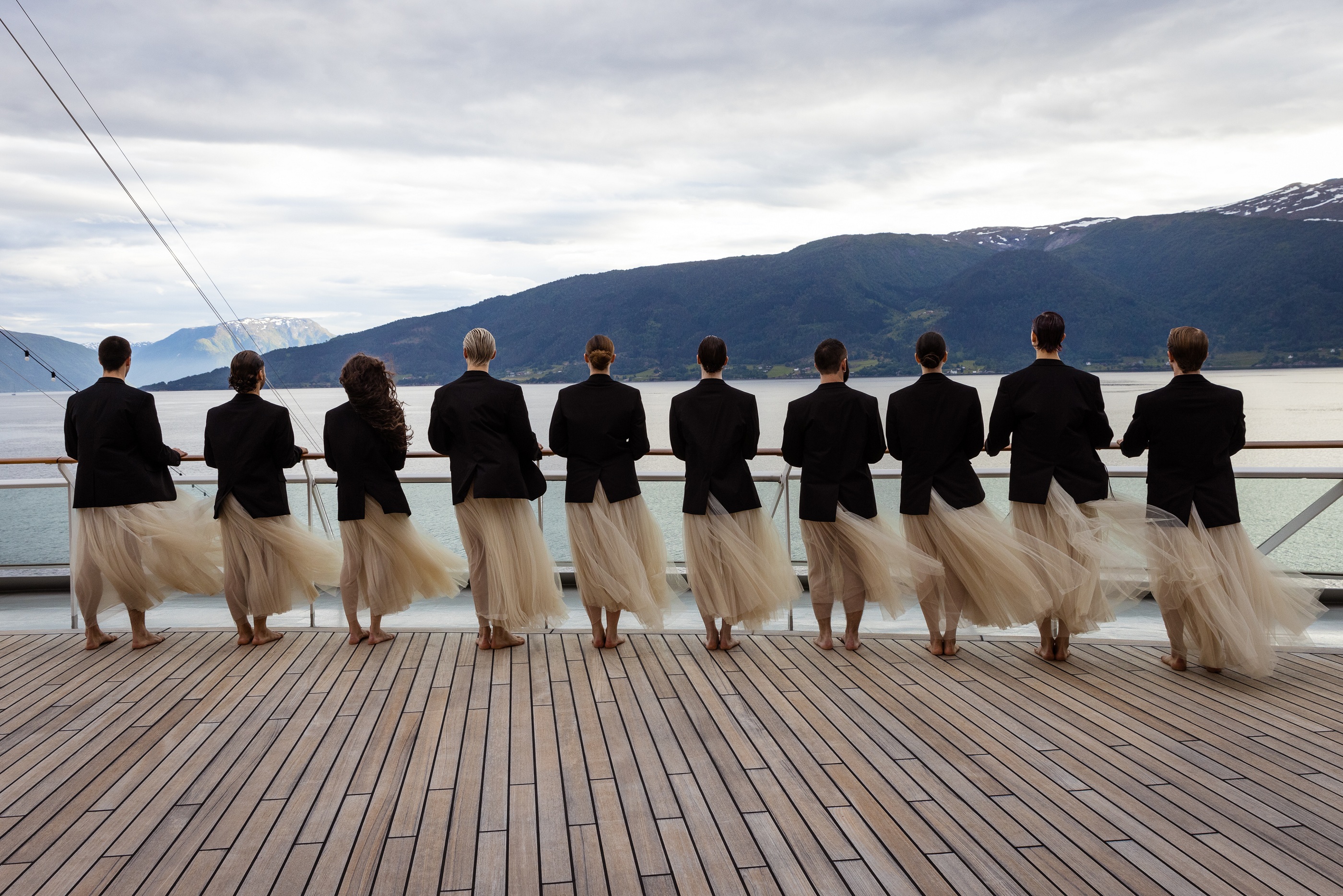 Zehn Tänzer des Choreografen Ekman stehen an der Reling der EUROPA 2 mit Blick auf eine Berglandschaft.