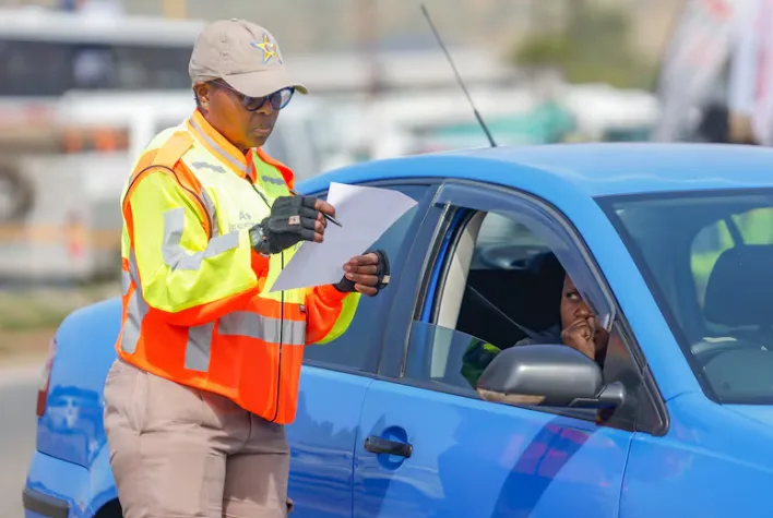 A South African traffic officer looking at a written infringement notice during a roadside stop, which demonstrates the first step in how AARTO demerit points work. A South African traffic officer looking at a written infringement notice during a roadside stop, which demonstrates the first step in how AARTO demerit points work.