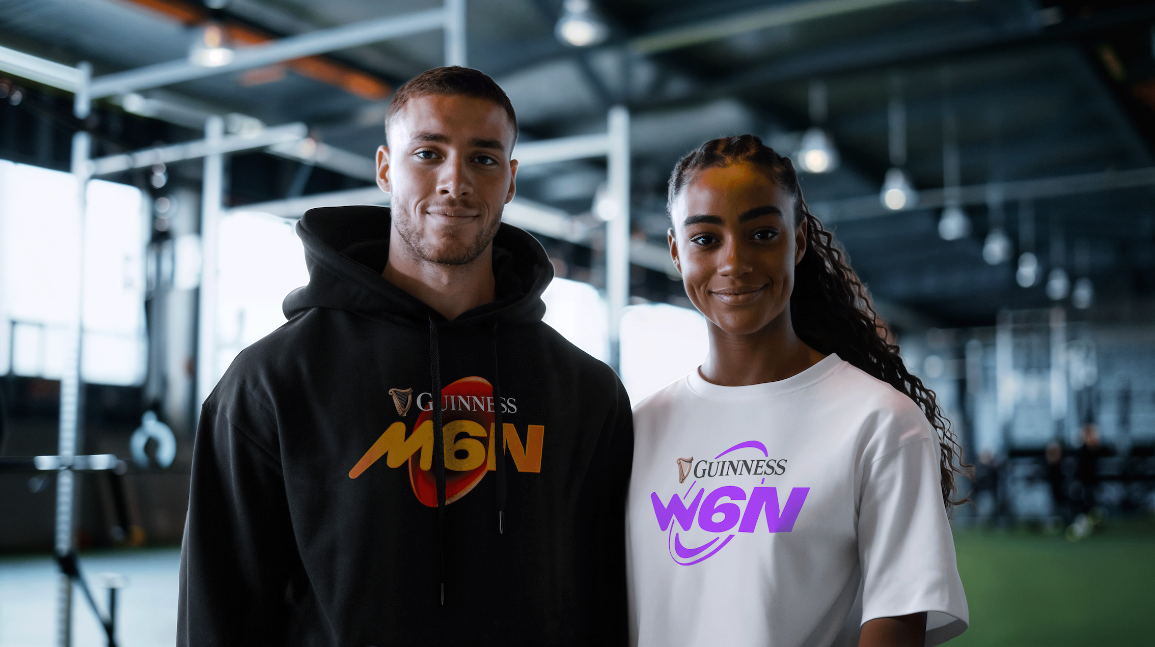 A man and a woman pose wearing a black Guinness Men's Six Nations and white Women's Six Nations hoodie respectively.
