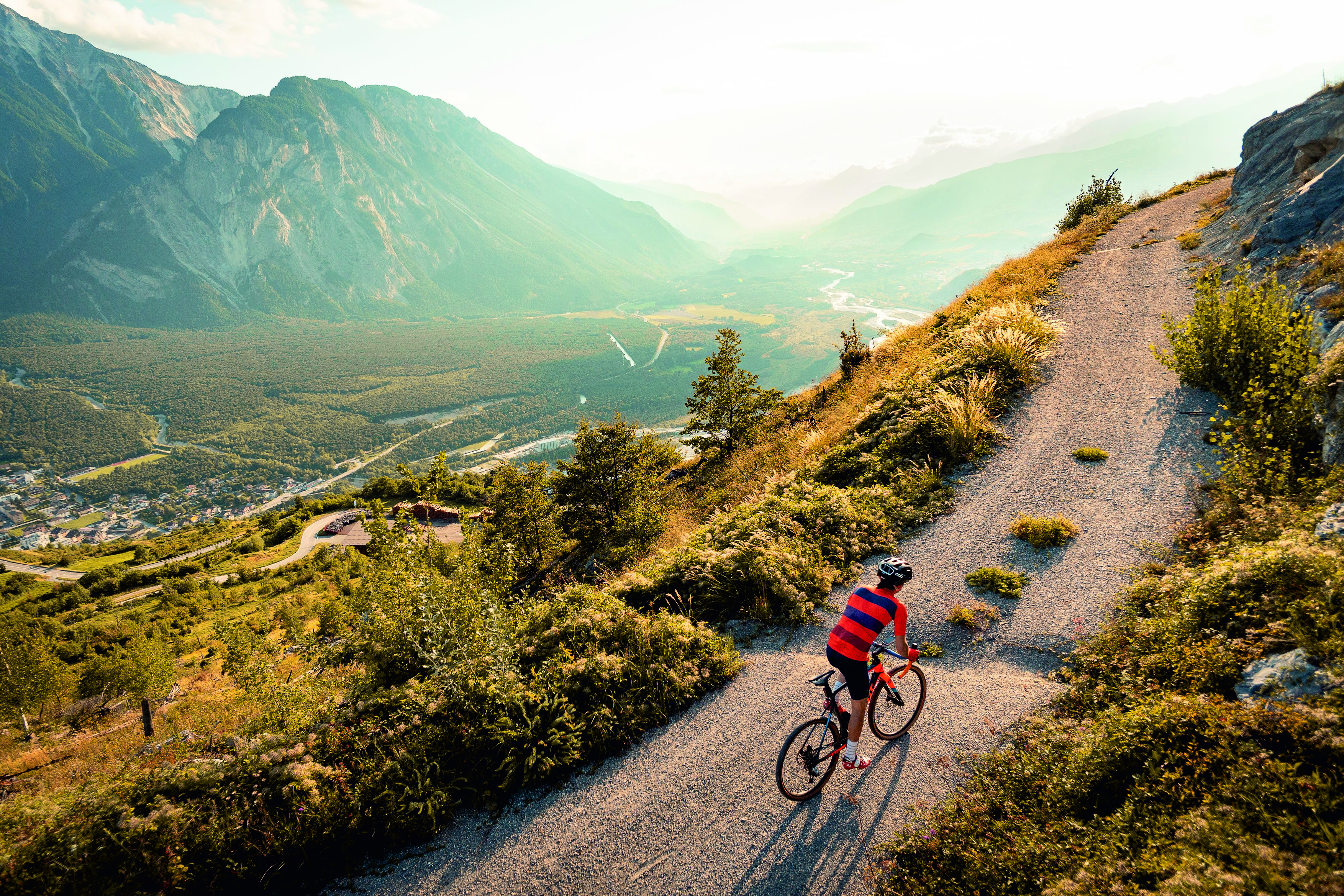 Person gravel biking on a mountain trail above Leuk with view over the Rhône Valley, Valais, Switzerland