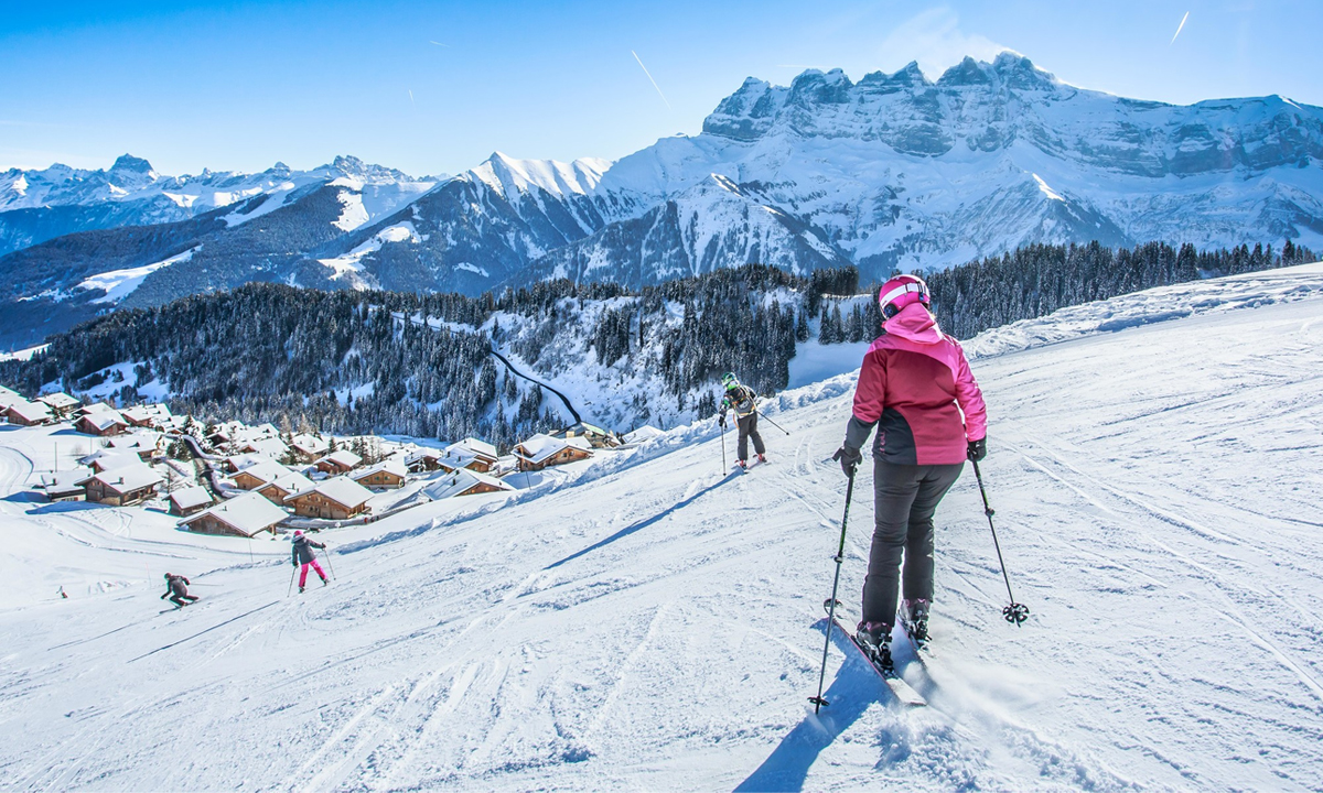 Eine Skifahrerin fährt die Piste Sépaya in Morgins hinunter, mit den majestätischen Dents du Midi im Hintergrund.