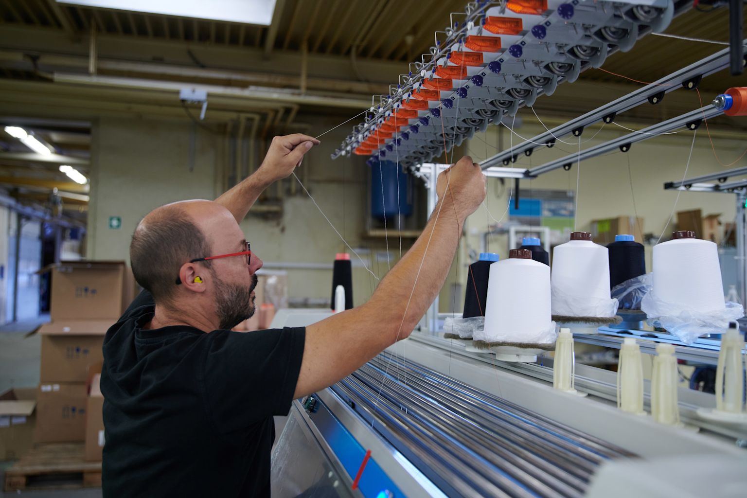 Bruno Neves checks a machine to see if the thread guide is running correctly, Valais, Switzerland
