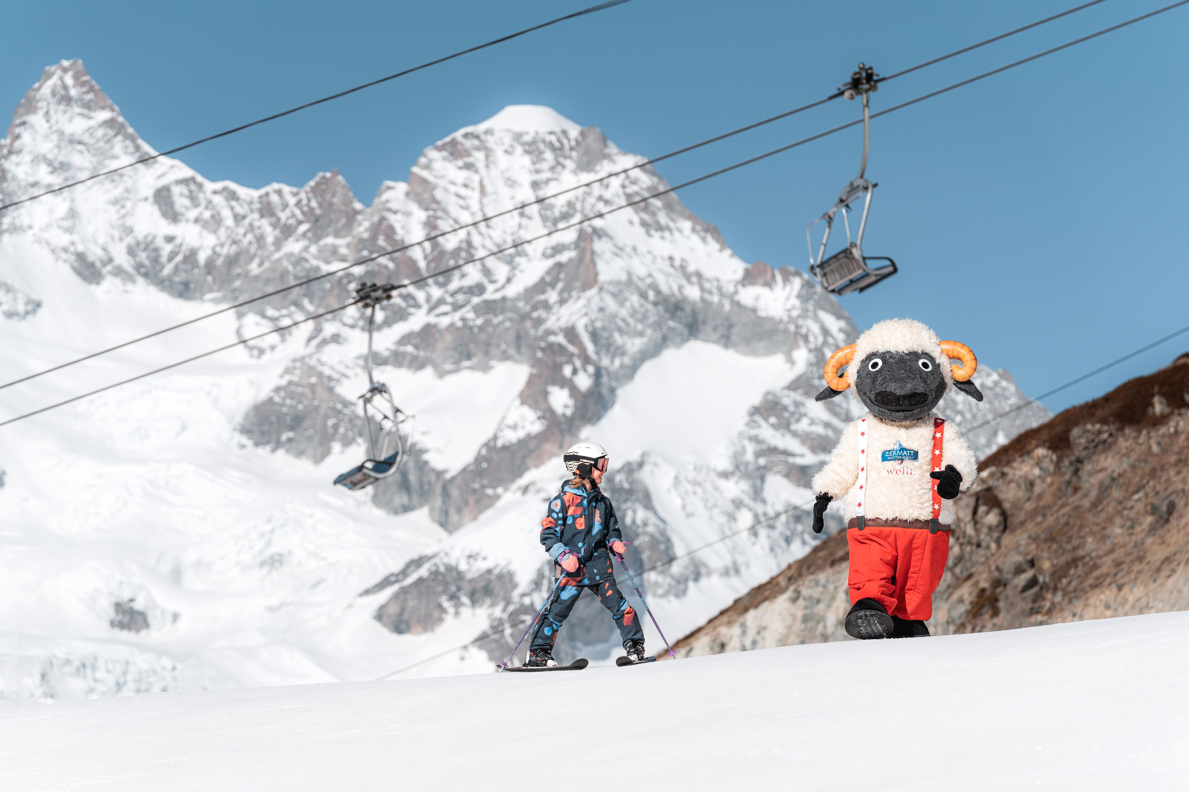 Skifahrendes Kind mit Wolli-Maskottchen und dem Matterhorn im Hintergrund