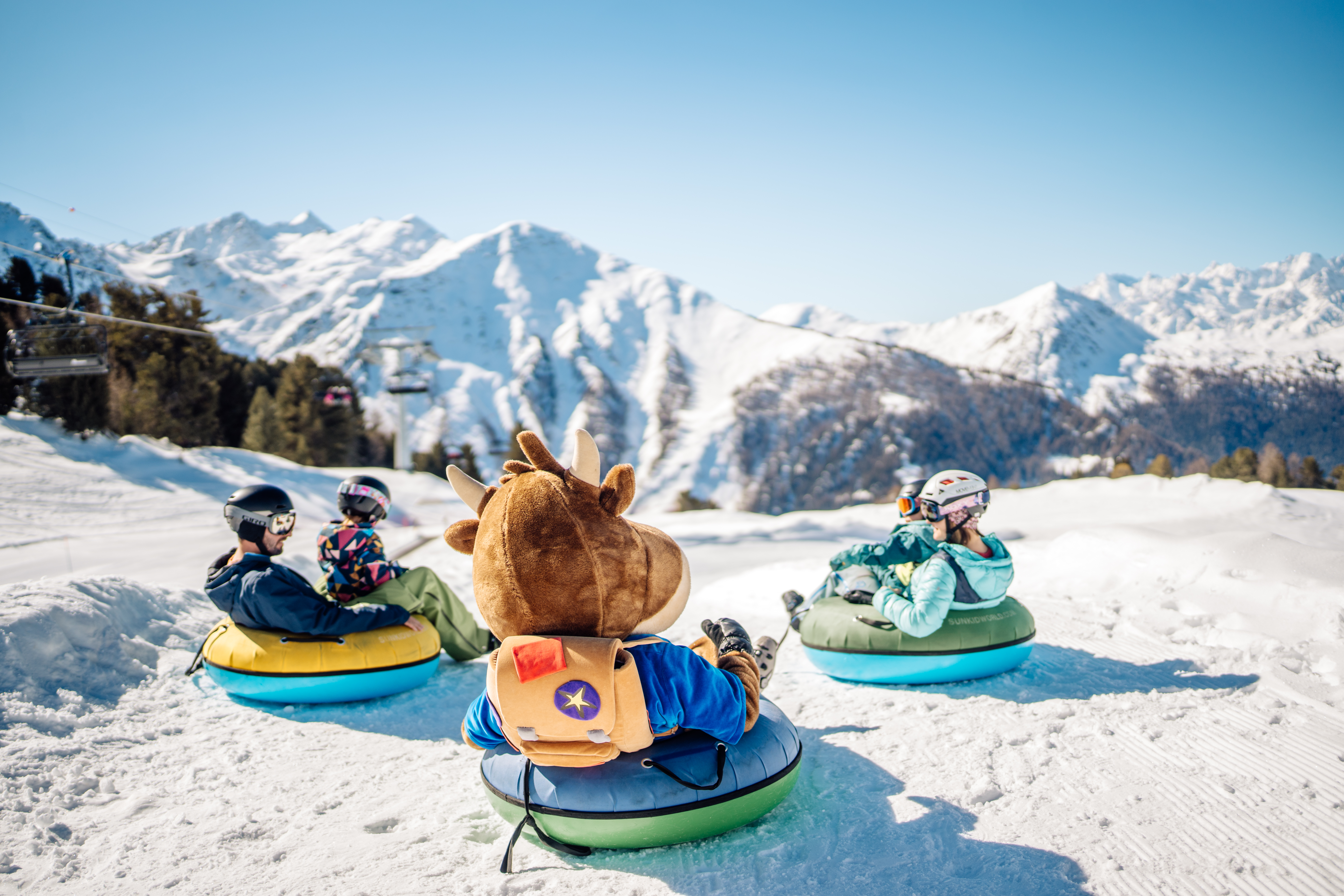 Mascot and children on snowtubes in the Tracouet snow park, surrounded by snowy mountains