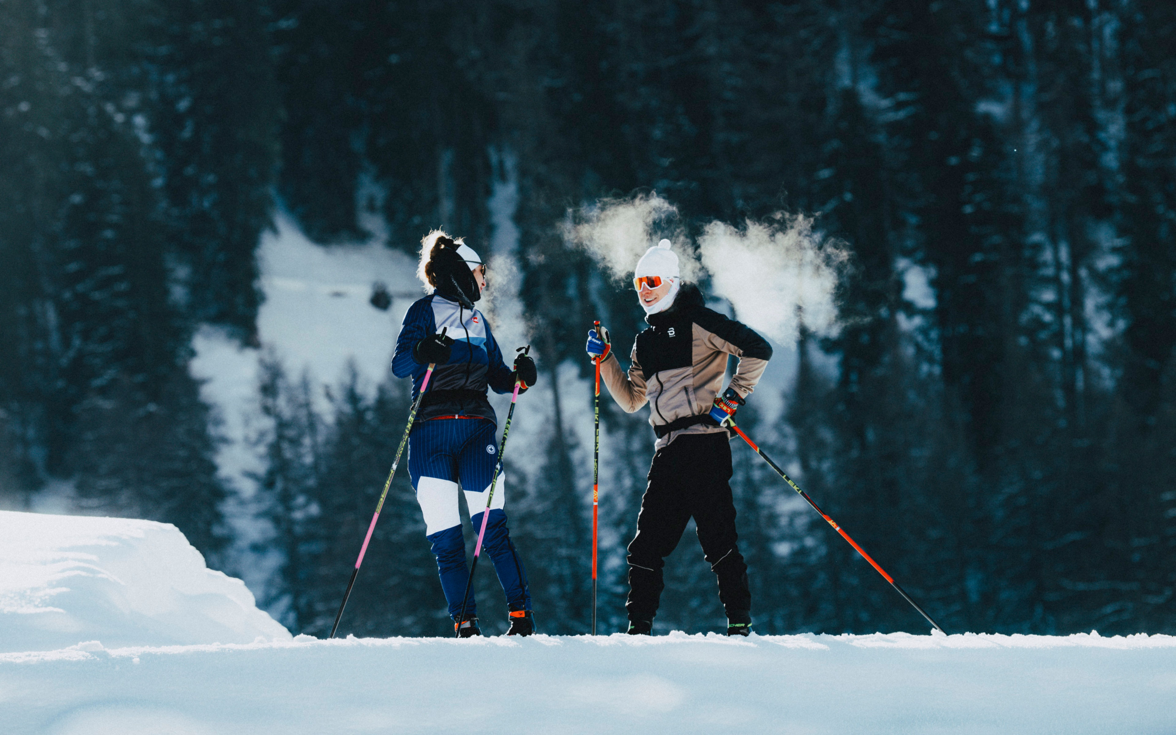 Zwei Langläufer sprechen miteinander auf der sonnigen Loipe in Goms, ihr Atem sichtbar in der kalten Luft