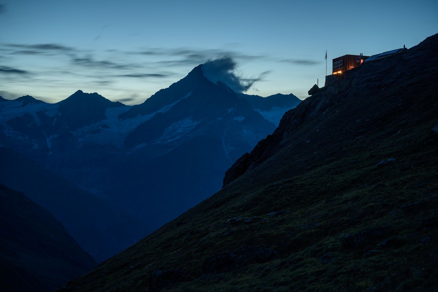 La cabane de Täsch dans la lumière du soleil couchant. A l’arrière-plan, dans les nuages, le Weisshorn.