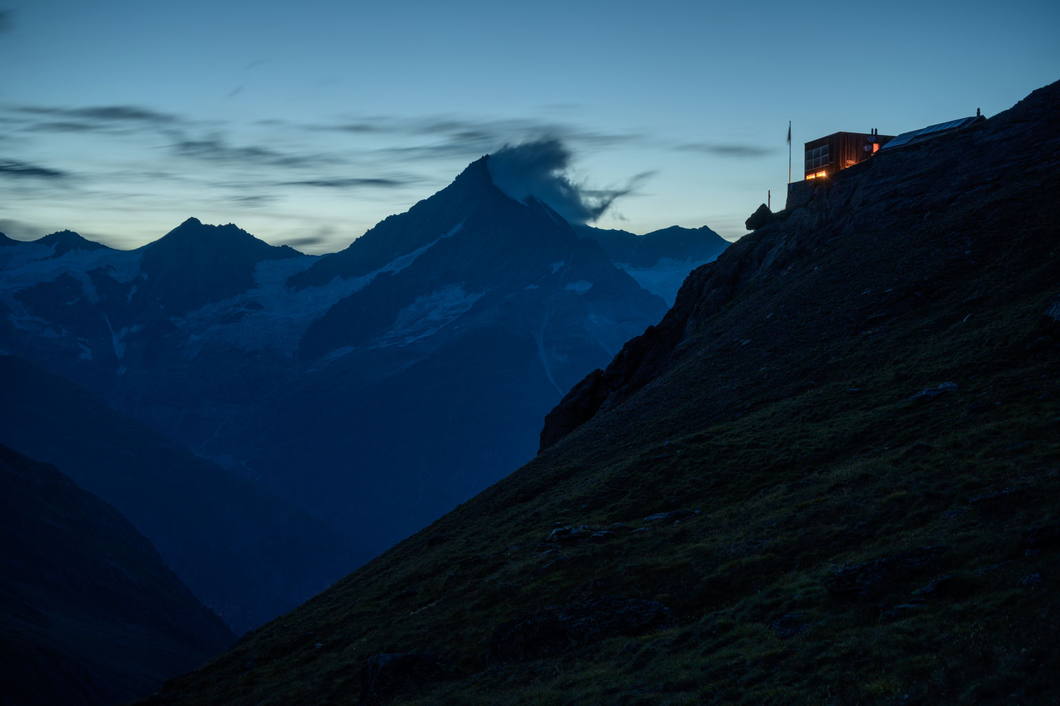 The Täschhütte mountain hut at sunset. In the distance, wreathed in cloud, the Weisshorn.