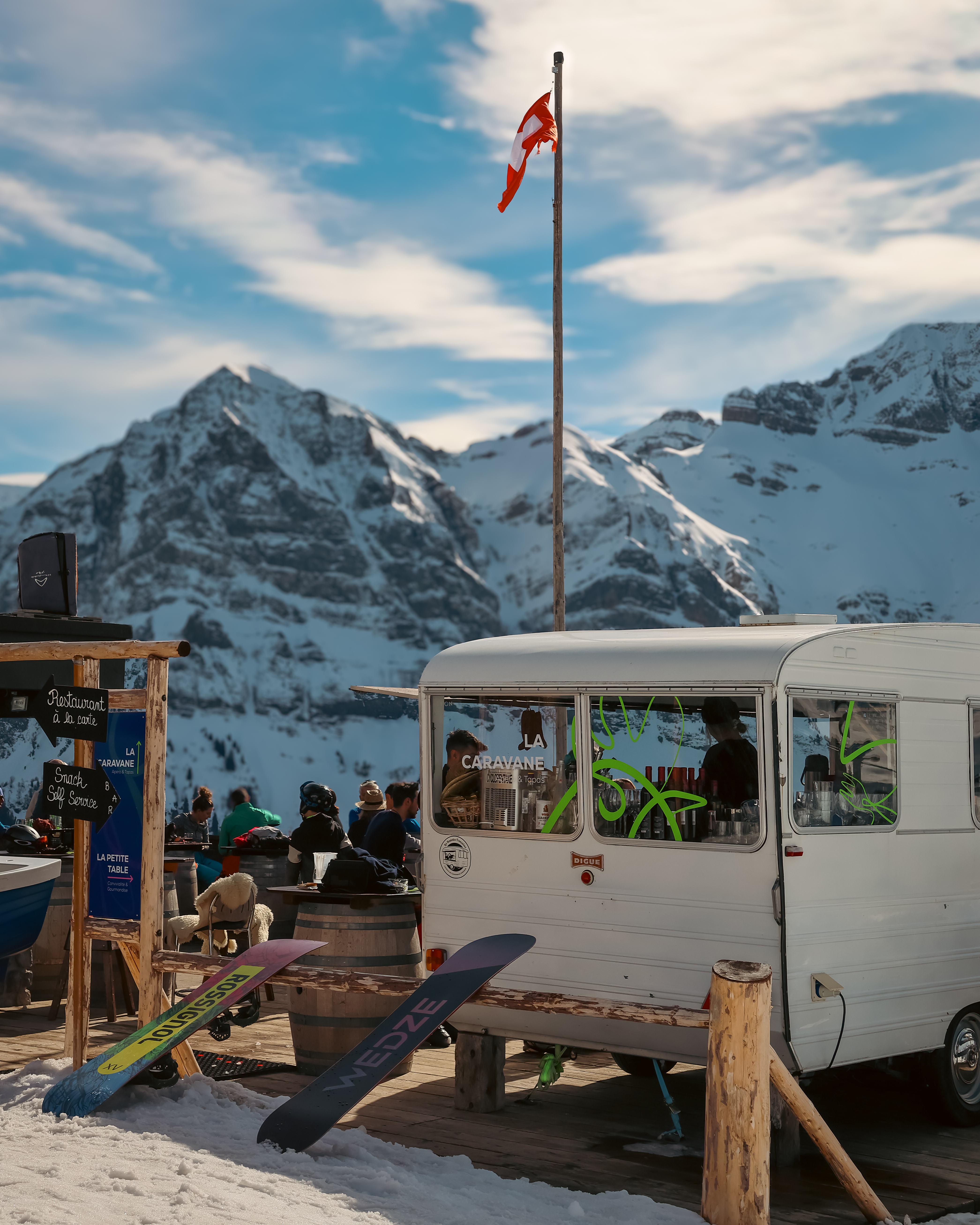 Weißer Wohnwagen vor verschneiten Bergen beim Restaurant Chez Coquoz in Champéry