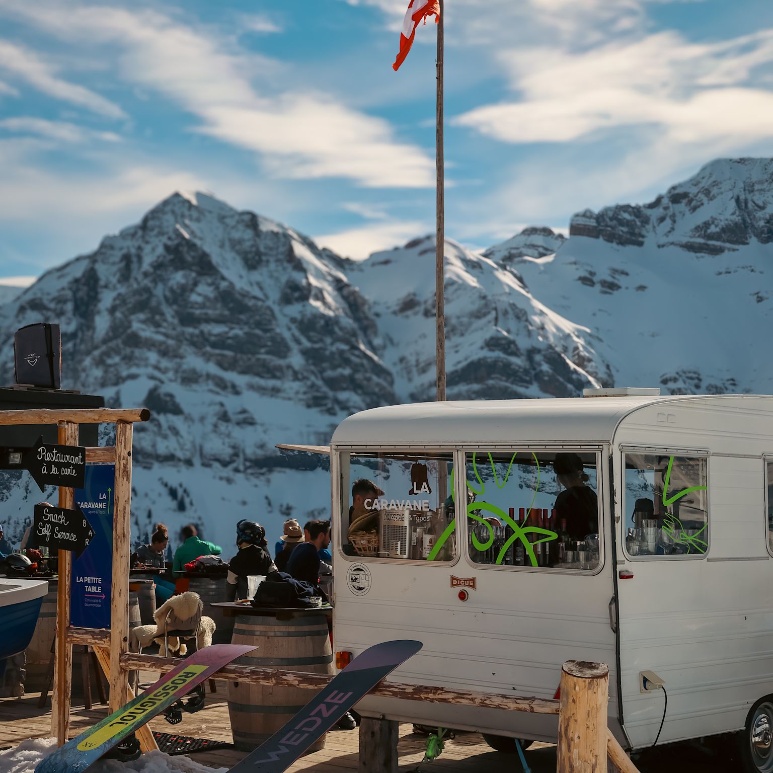Weißer Wohnwagen vor verschneiten Bergen beim Restaurant Chez Coquoz in Champéry