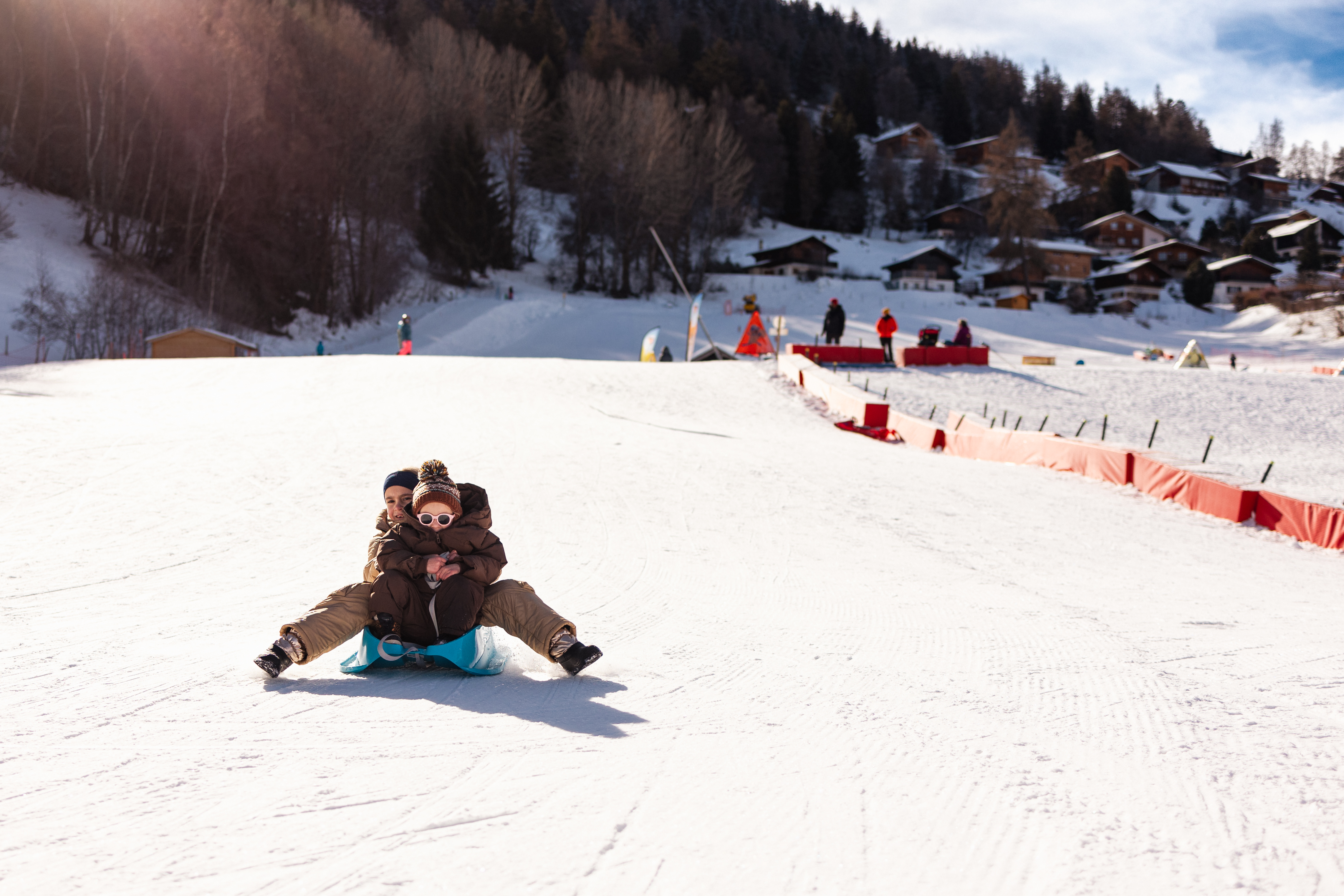 Un adulte et un enfant faisant de la luge ensemble dans l’espace débutants Le Lavioz à Vercorin, en Valais, sur une piste enneigée damée.