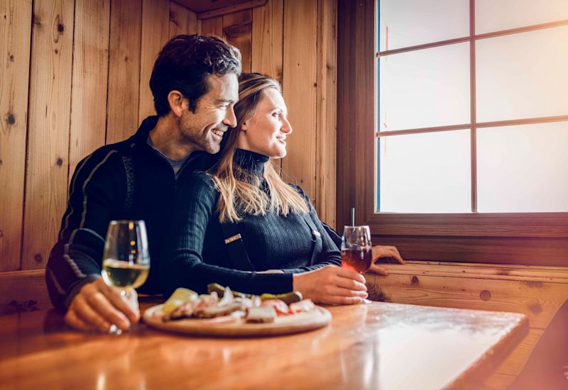 Un couple prend l'apéro (vin valaisan et planchette valaisanne) en observant la vue après une belle journée de ski sur les pistes de Crans-Montana. Valais, Suisse