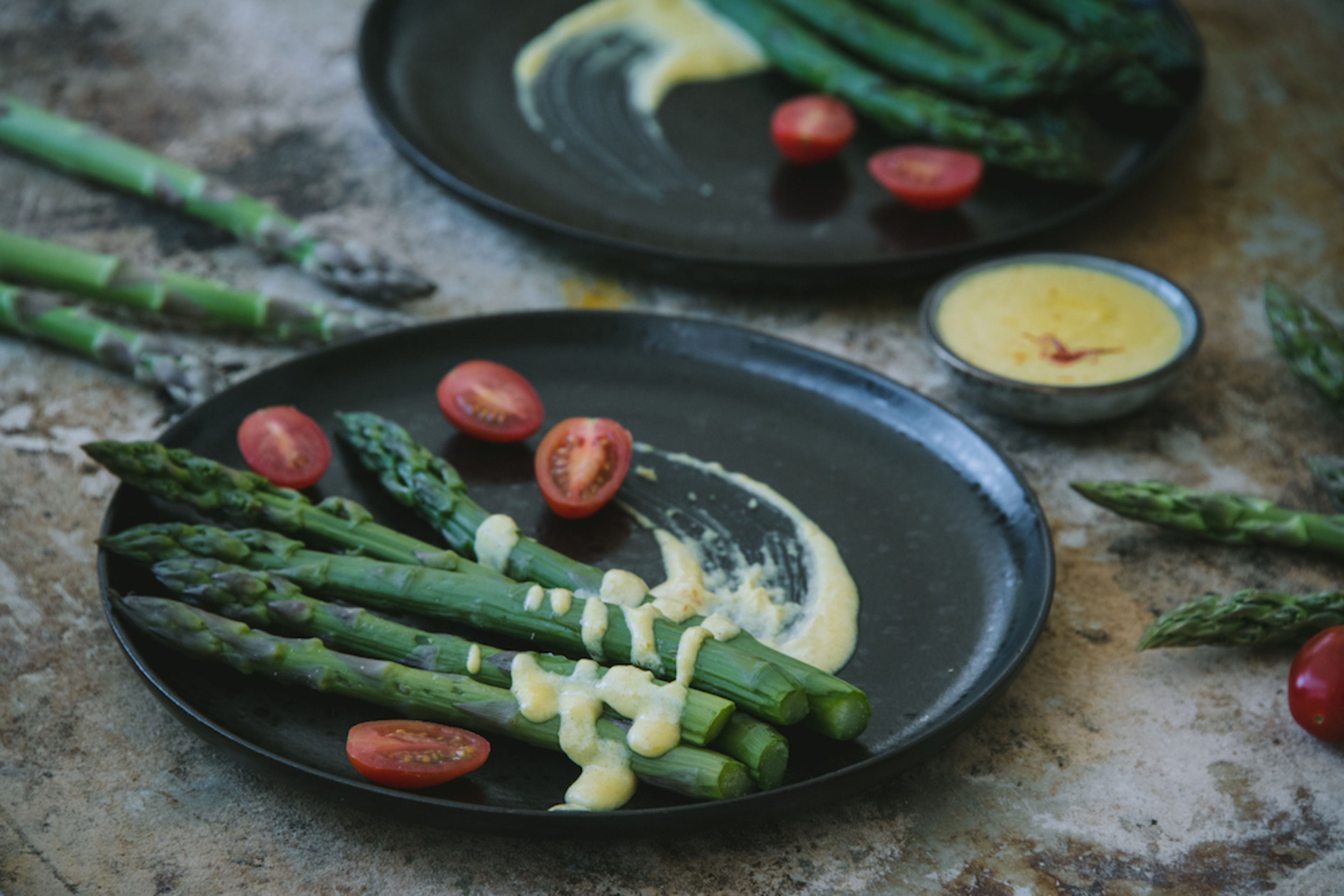 Asperges vertes servies avec une sauce au safran et des tomates cerises sur des assiettes noires