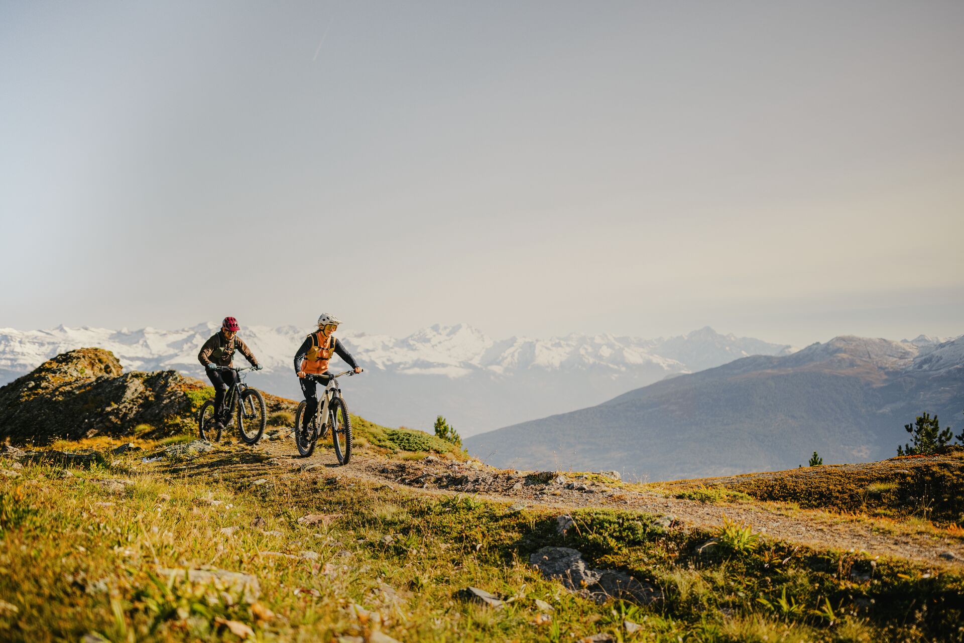 Two mountain bikers riding along a trail in Val d’Hérens with a view of the Valais Alps