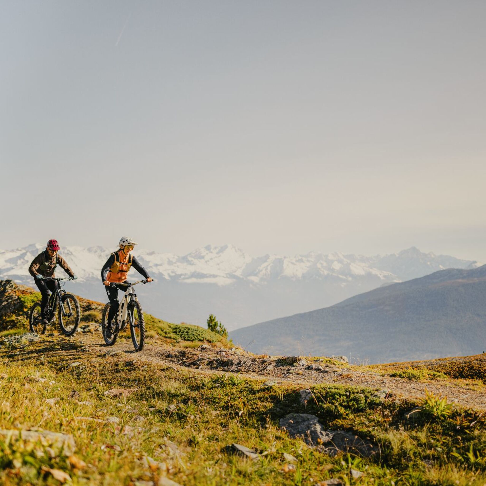 Two mountain bikers riding along a trail in Val d’Hérens with a view of the Valais Alps