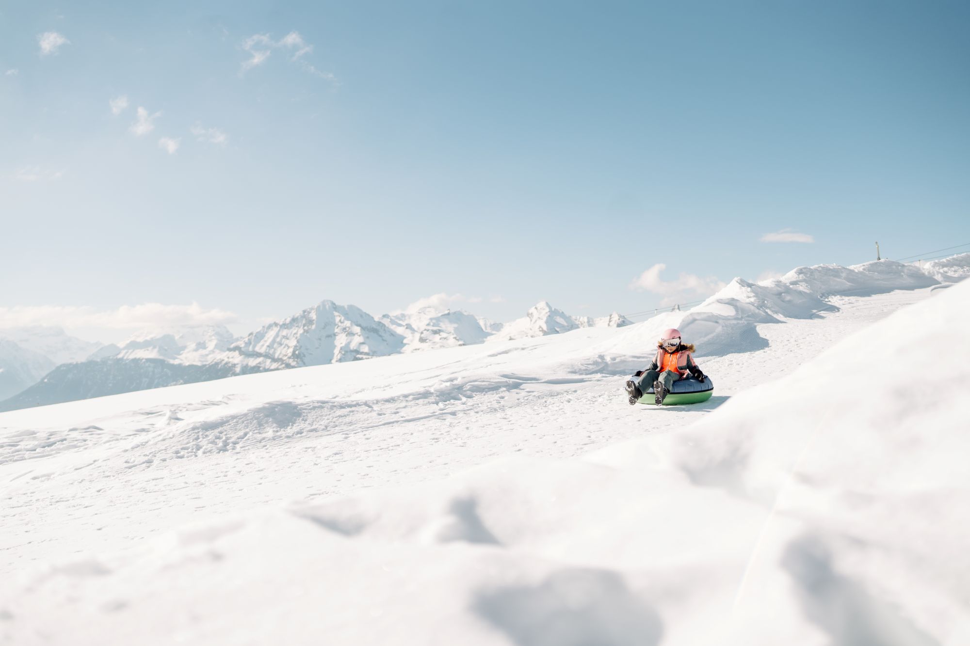 Child riding alone on a snowtube in the snow with mountains in the background