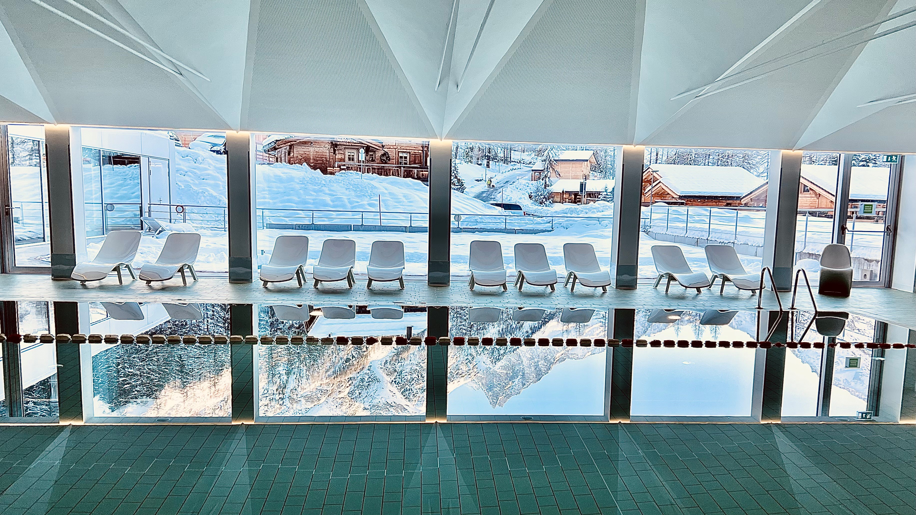 Modernes Hallenbad mit Liegestühlen und großen Fenstern in Zinal, umgeben von verschneiten Chalets