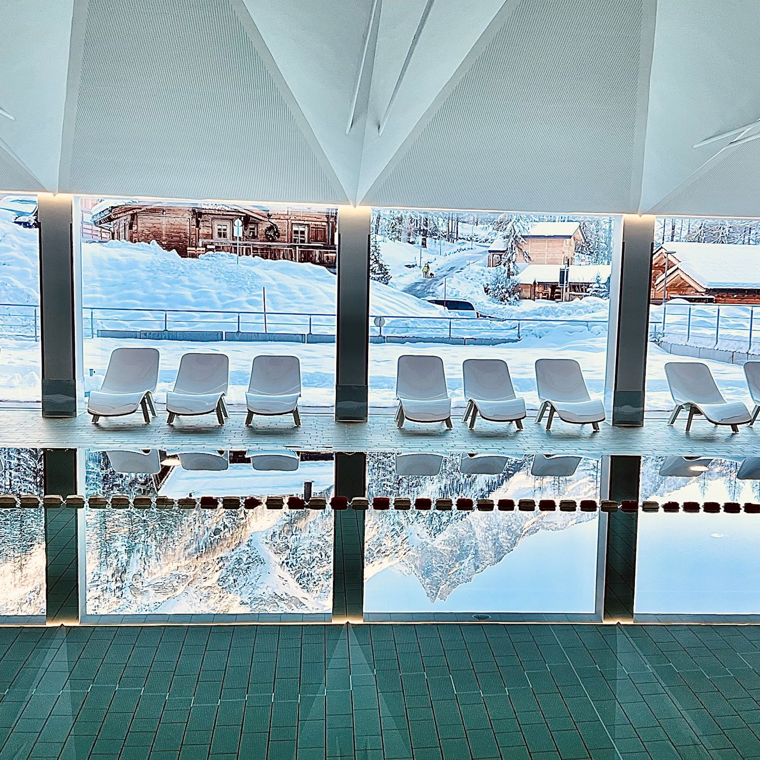 Modernes Hallenbad mit Liegestühlen und großen Fenstern in Zinal, umgeben von verschneiten Chalets