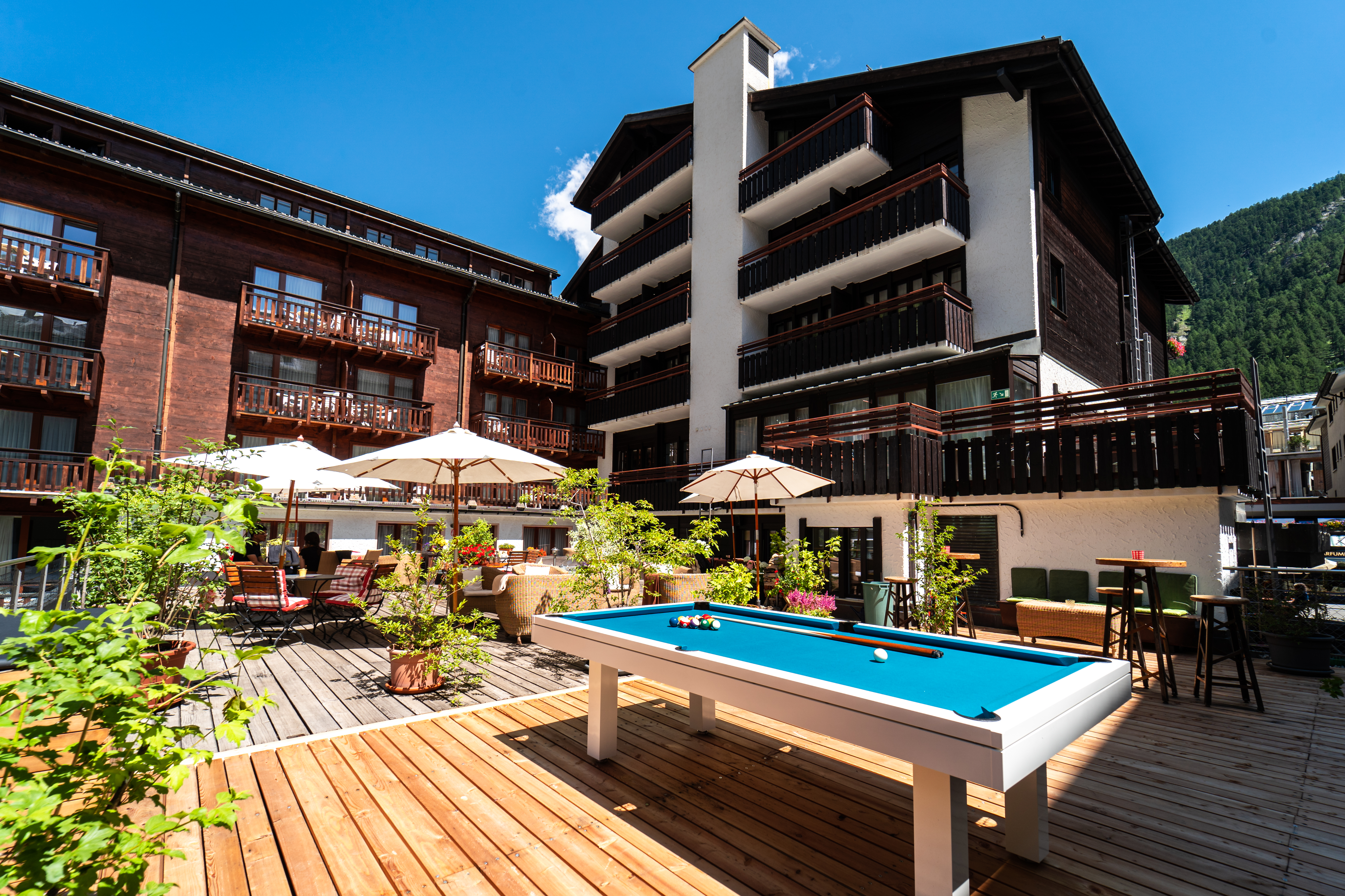 Gemütliche Terrasse im Hotel Pollux in Zermatt mit Sonnenschirmen, Sitzgelegenheiten und Billardtisch