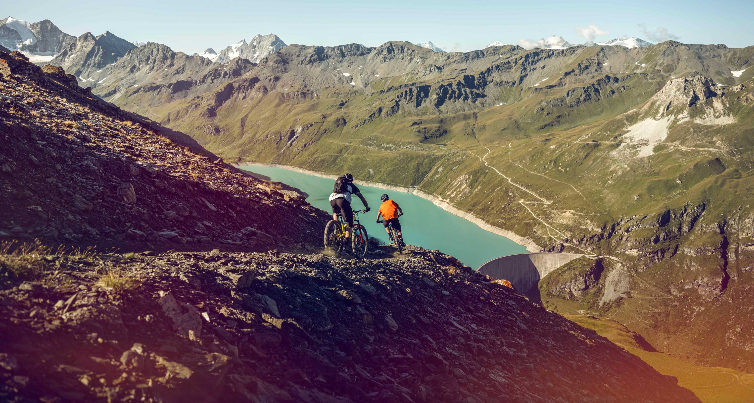 Zwei Mountainbiker bei der Abfahrt einer Mountainbike-Route mit Blick auf den Lac de Moiry. Wallis, Schweiz