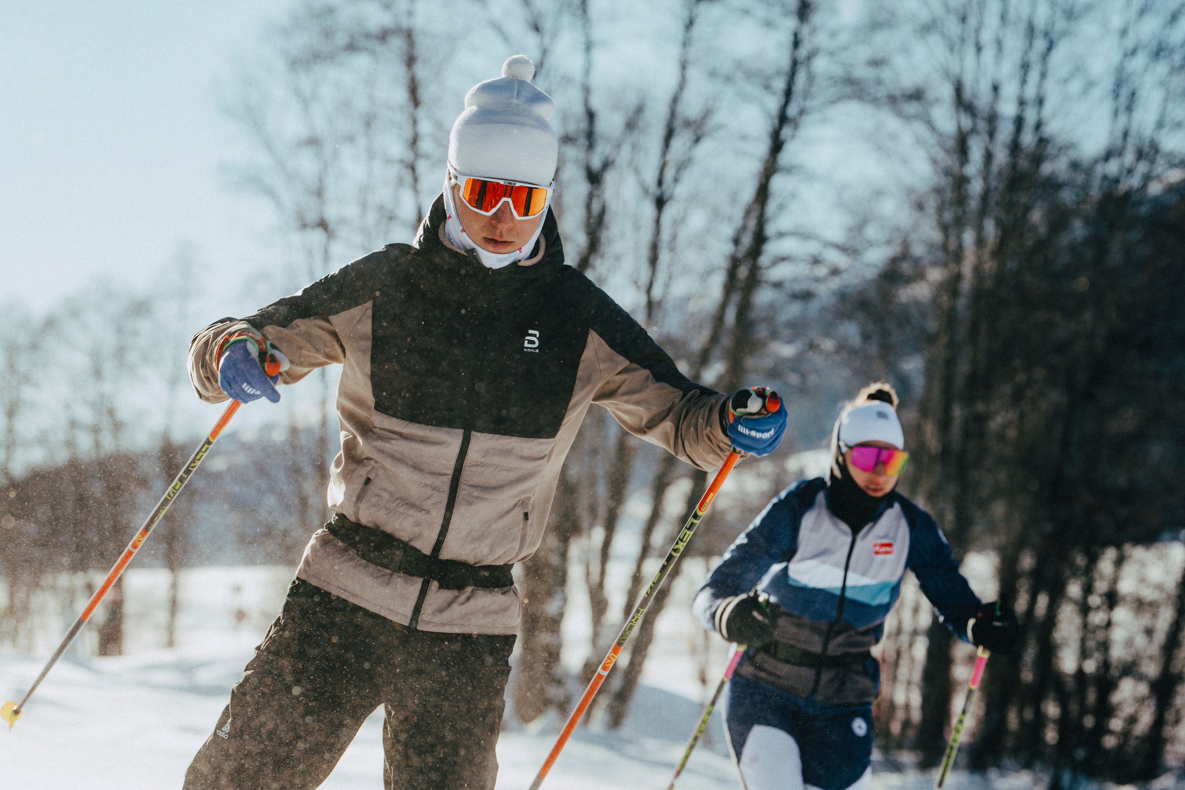 Two cross-country skiers training in the sunny and snowy Goms landscape