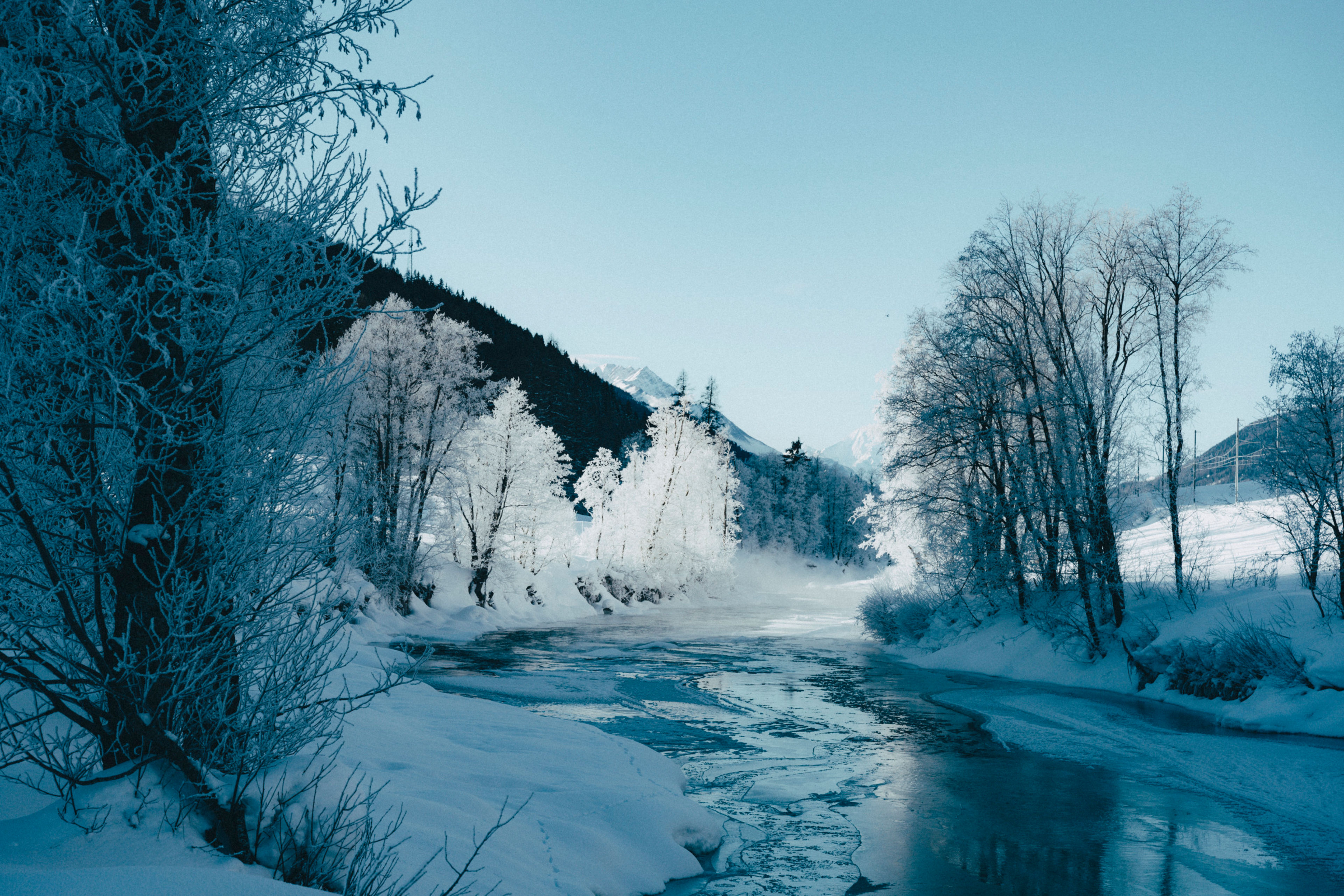 Der Rotten fliesst ruhig durch die verschneite Landschaft von Goms, umgeben von vereisten Bäumen