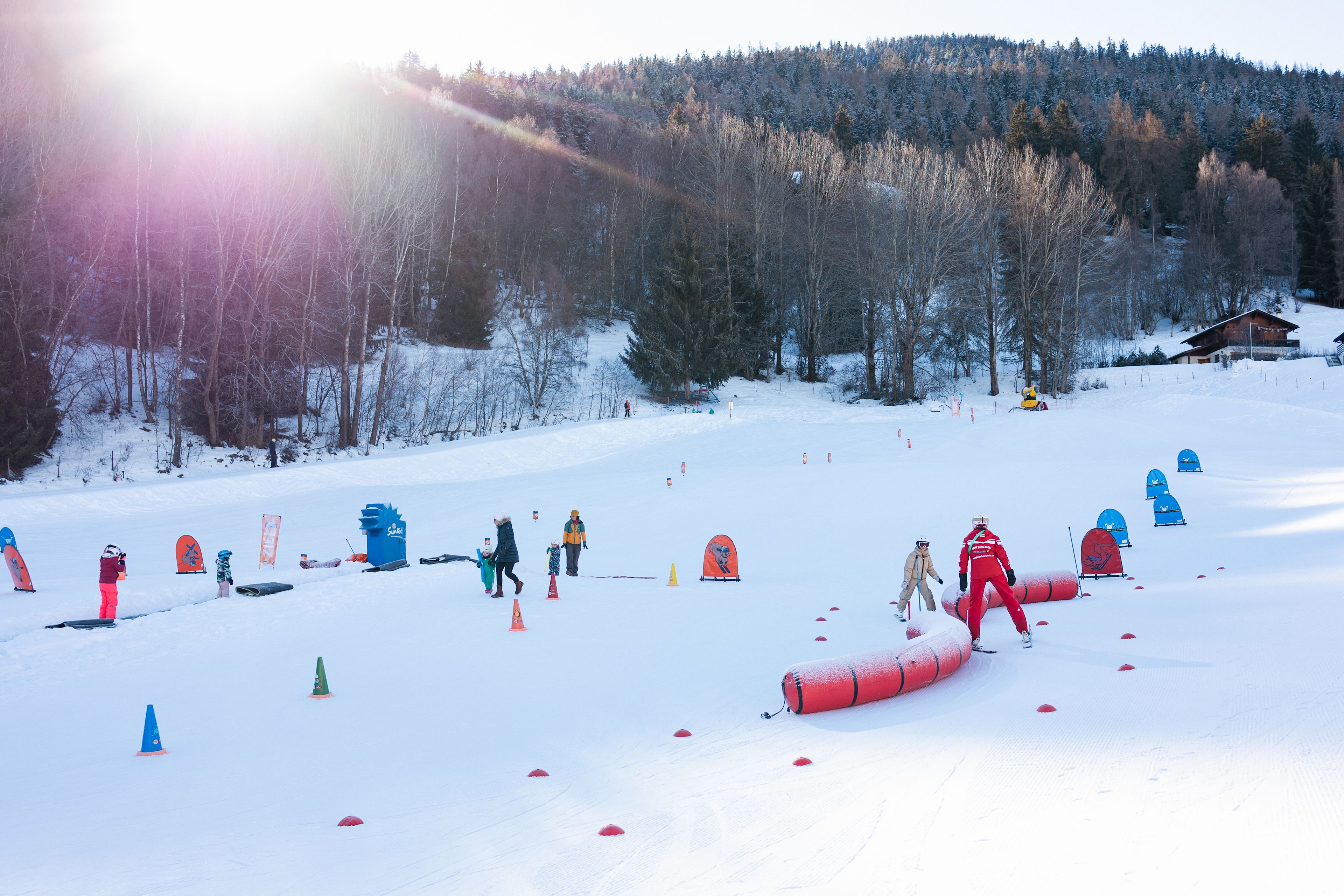 Skilehrer und Anfänger üben spielerisch das Skifahren im Anfängerbereich Le Lavioz in Vercorin, umgeben von einer verschneiten Winterlandschaft.