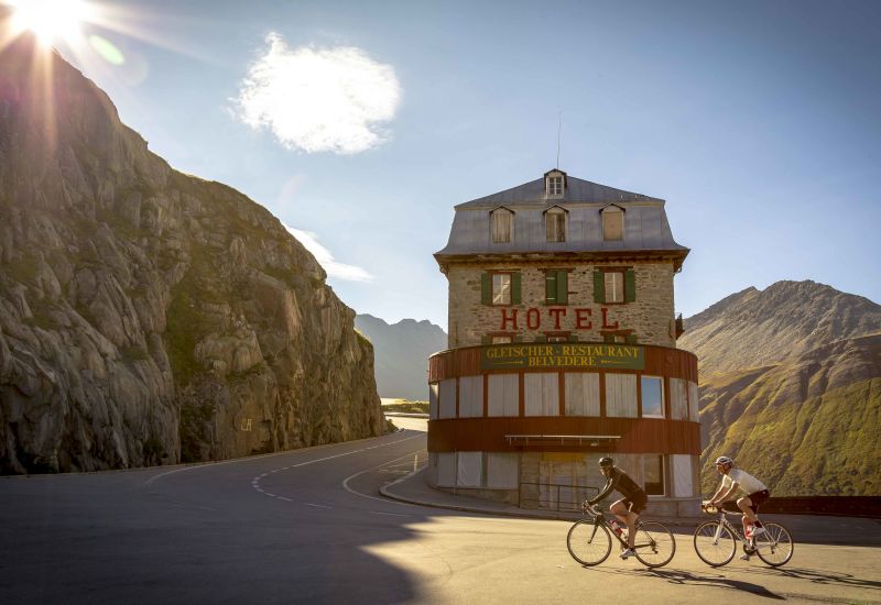 Zwei Radfahrer auf dem Furka-Anstieg fahren durch das Hotel Belvédère. Wallis, Schweiz