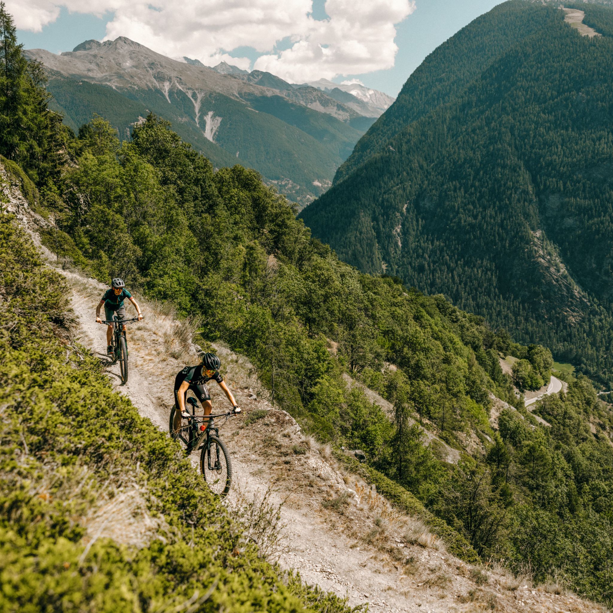 Two mountain bikers in full effort descending a mountain bike trail.  Valais, Switzerland.