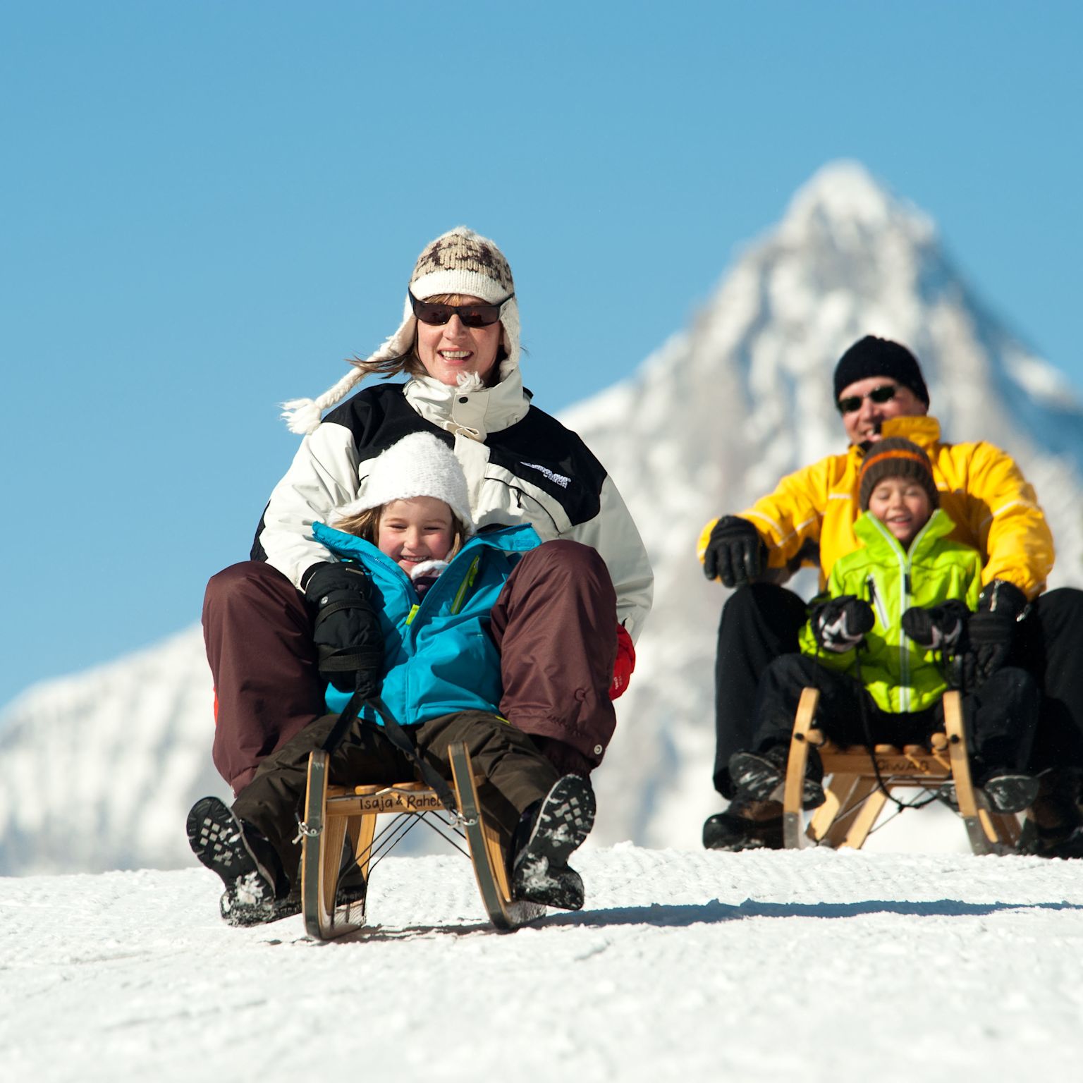Two families enjoying a thrilling toboggan ride on the Heidadorf sledding run in Visperterminen under sunny skies