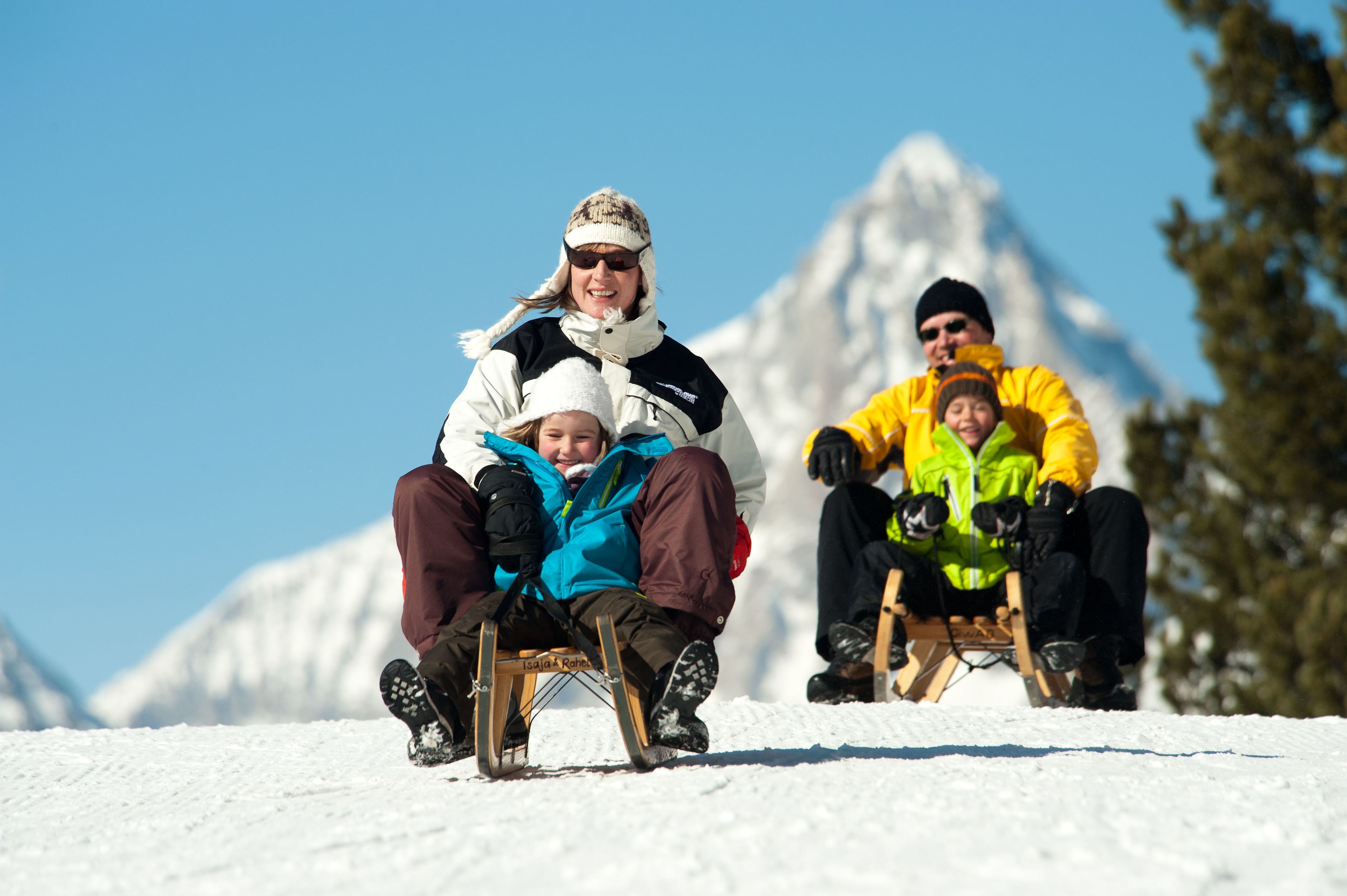 Two families enjoying a thrilling toboggan ride on the Heidadorf sledding run in Visperterminen under sunny skies