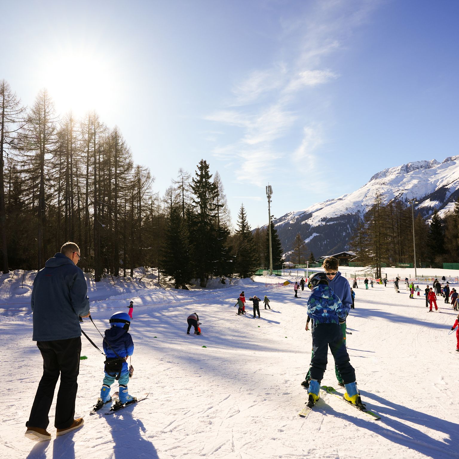 Enfants apprenant à skier dans le jardin des neiges ensoleillé de Bellwald avec accompagnement parental