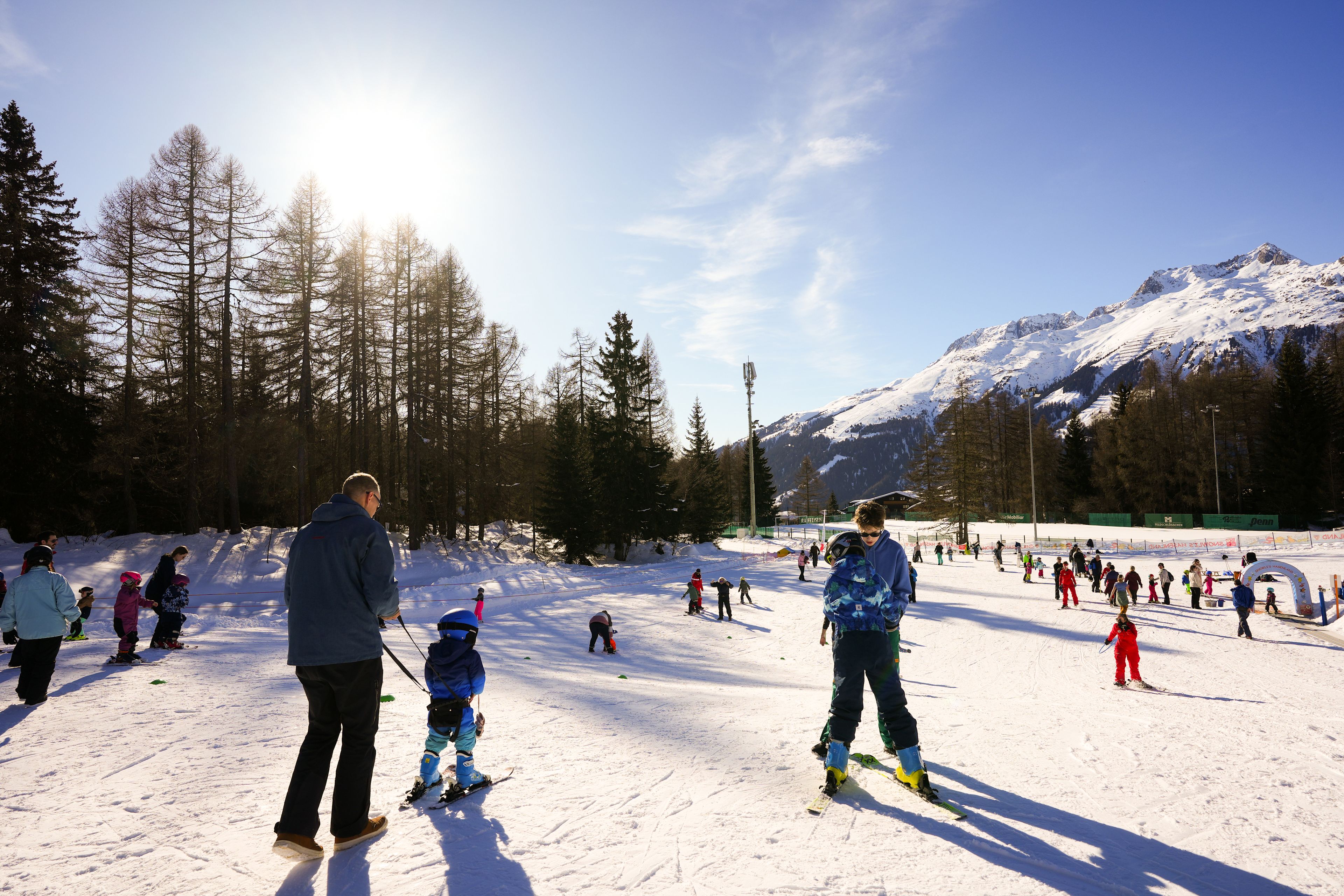 Enfants apprenant à skier dans le jardin des neiges ensoleillé de Bellwald avec accompagnement parental