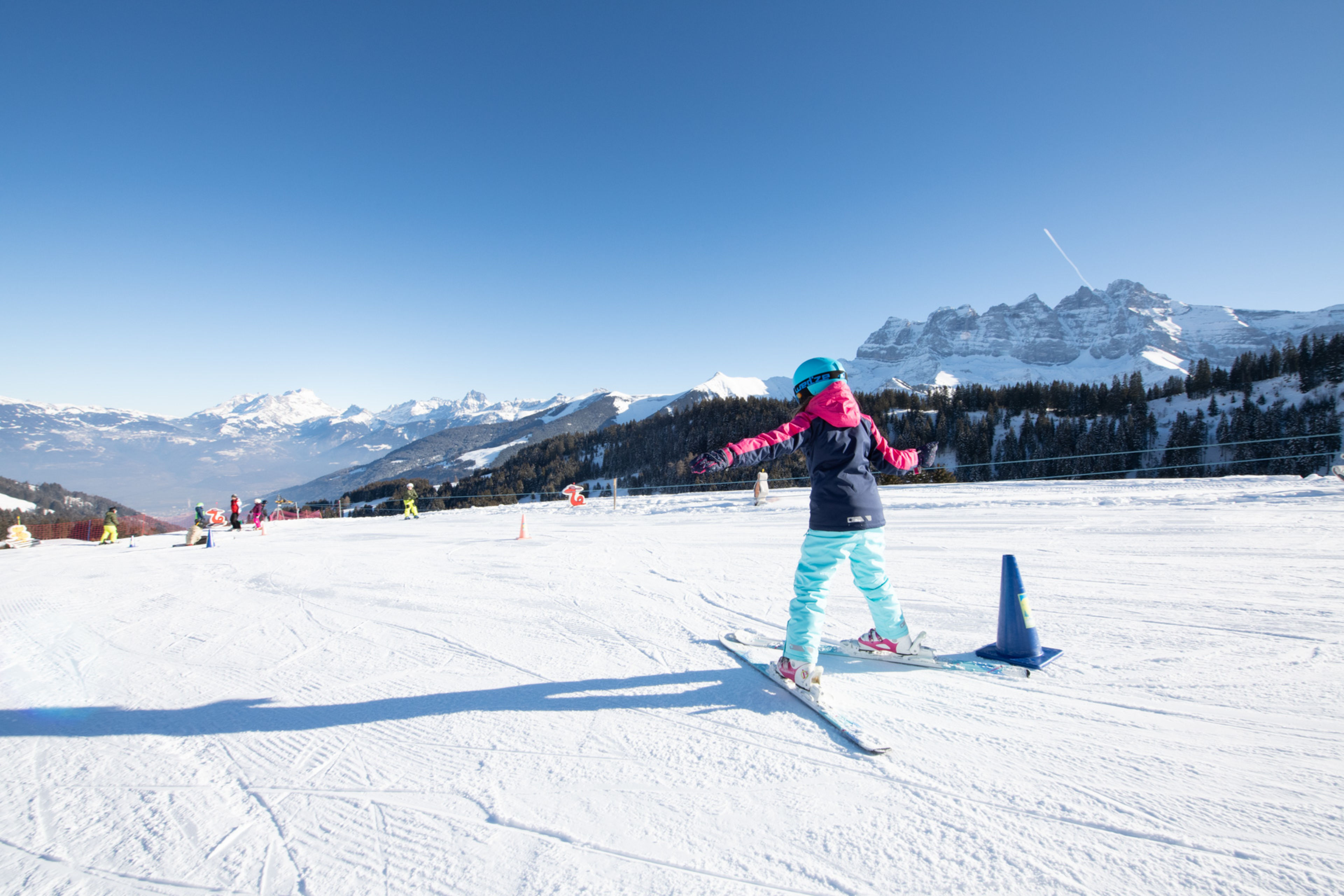 Ein Kind fährt die schneebedeckte Piste Sépaya in Morgins hinunter, mit den majestätischen Dents du Midi im Hintergrund.