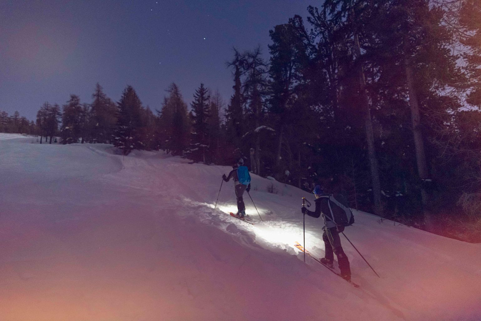 Two people ski touring at night, lit by their headlamps and the moon. Valais, Switzerland