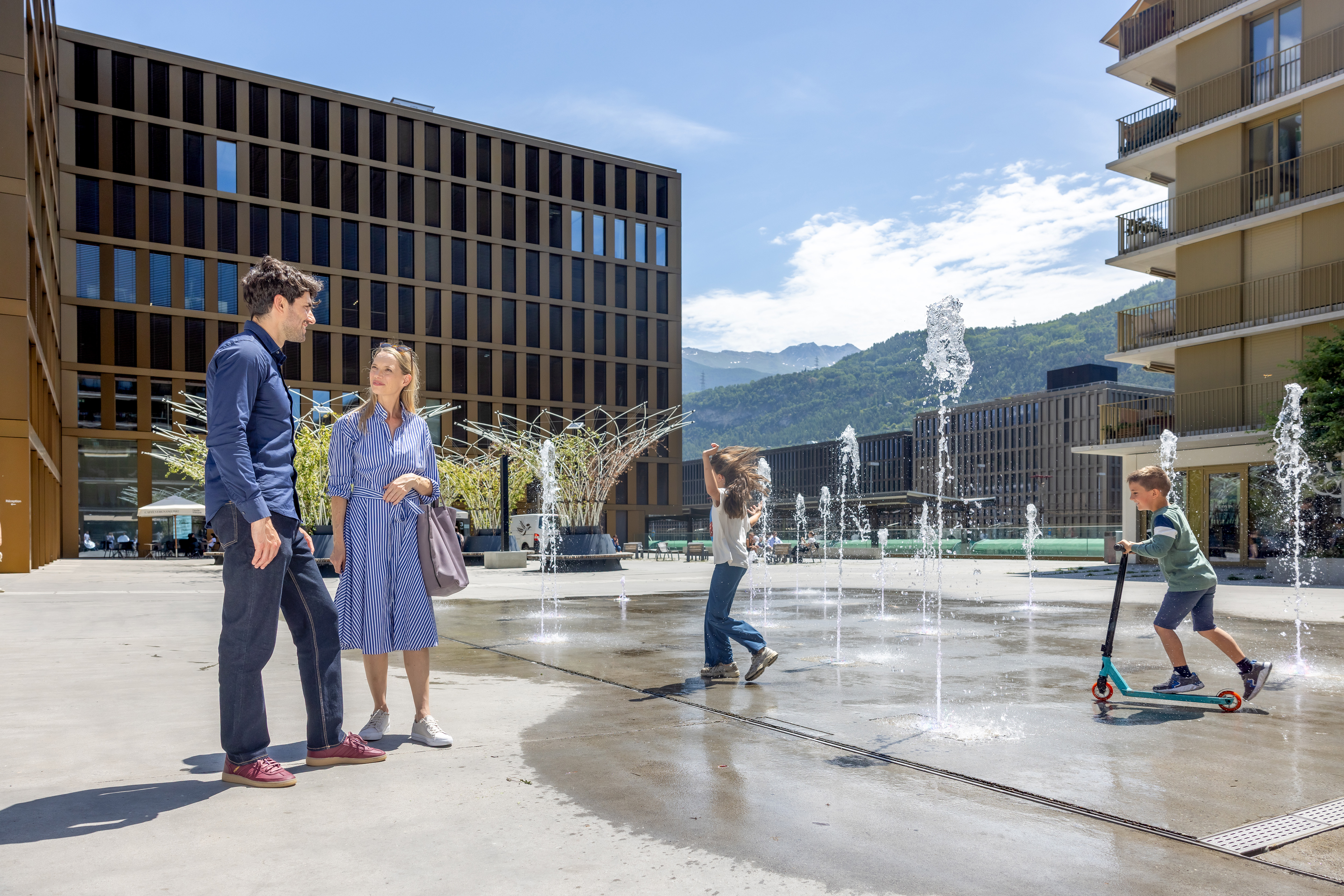 Famille et enfants sur une place avec jets d’eau à Sion, Valais, Suisse