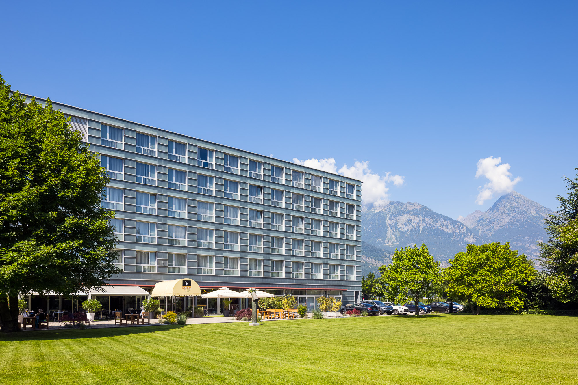Modernes Gebäude des Hotels Vatel in Martigny mit großer Gartenfläche und Alpenpanorama im Hintergrund