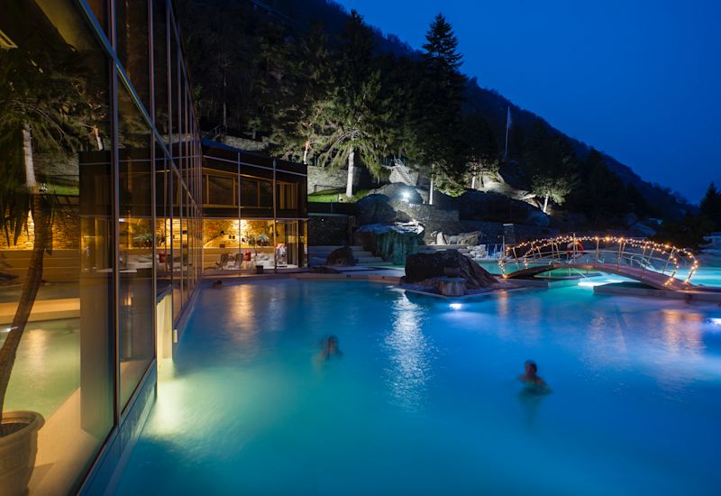Des gens se baignent le soir avec la lune aux bains thermaux de Brigerbad. Valais, Suisse