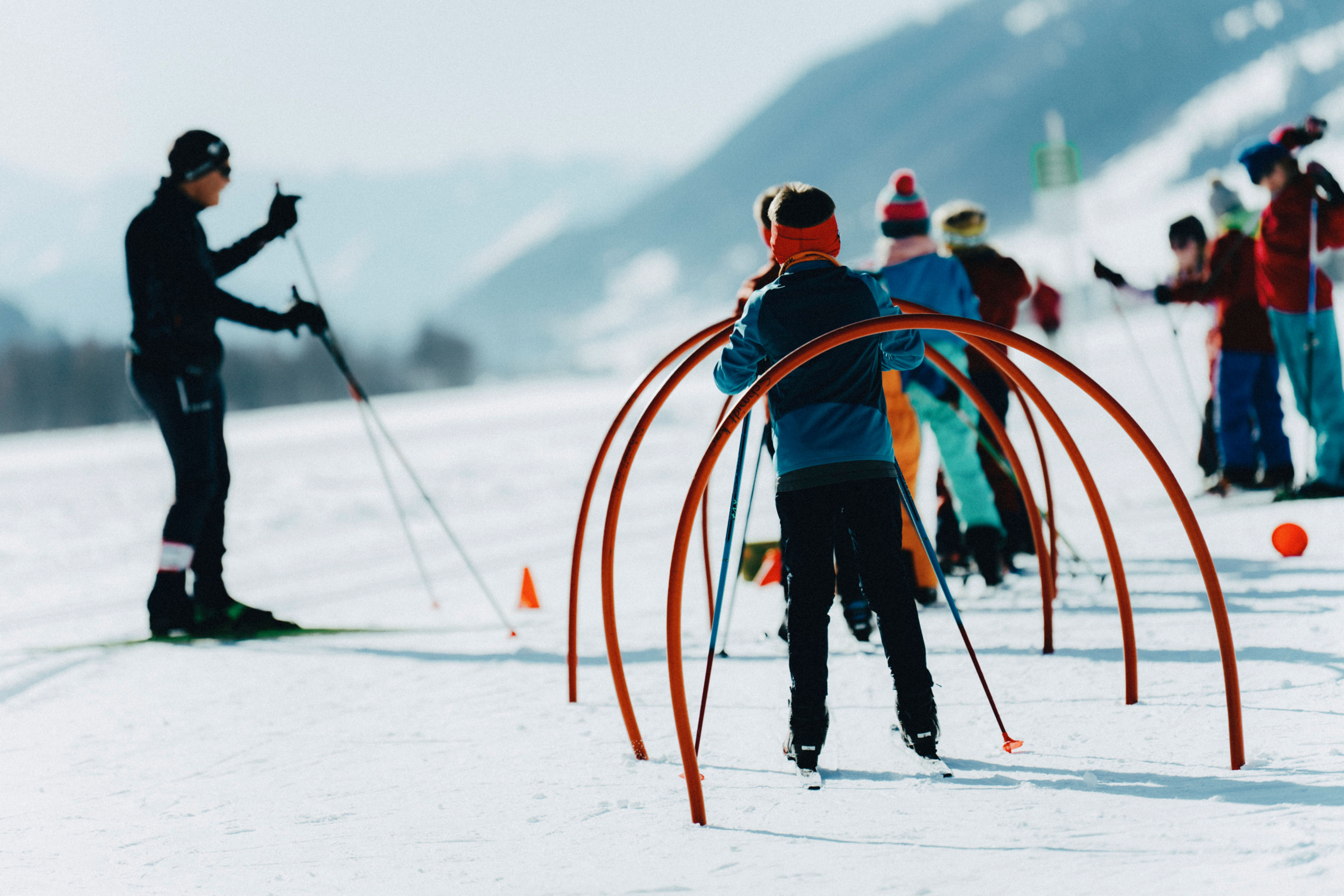 Kinder üben Langlauf unter Anleitung eines Trainers auf einem verschneiten Feld in Goms, Wallis