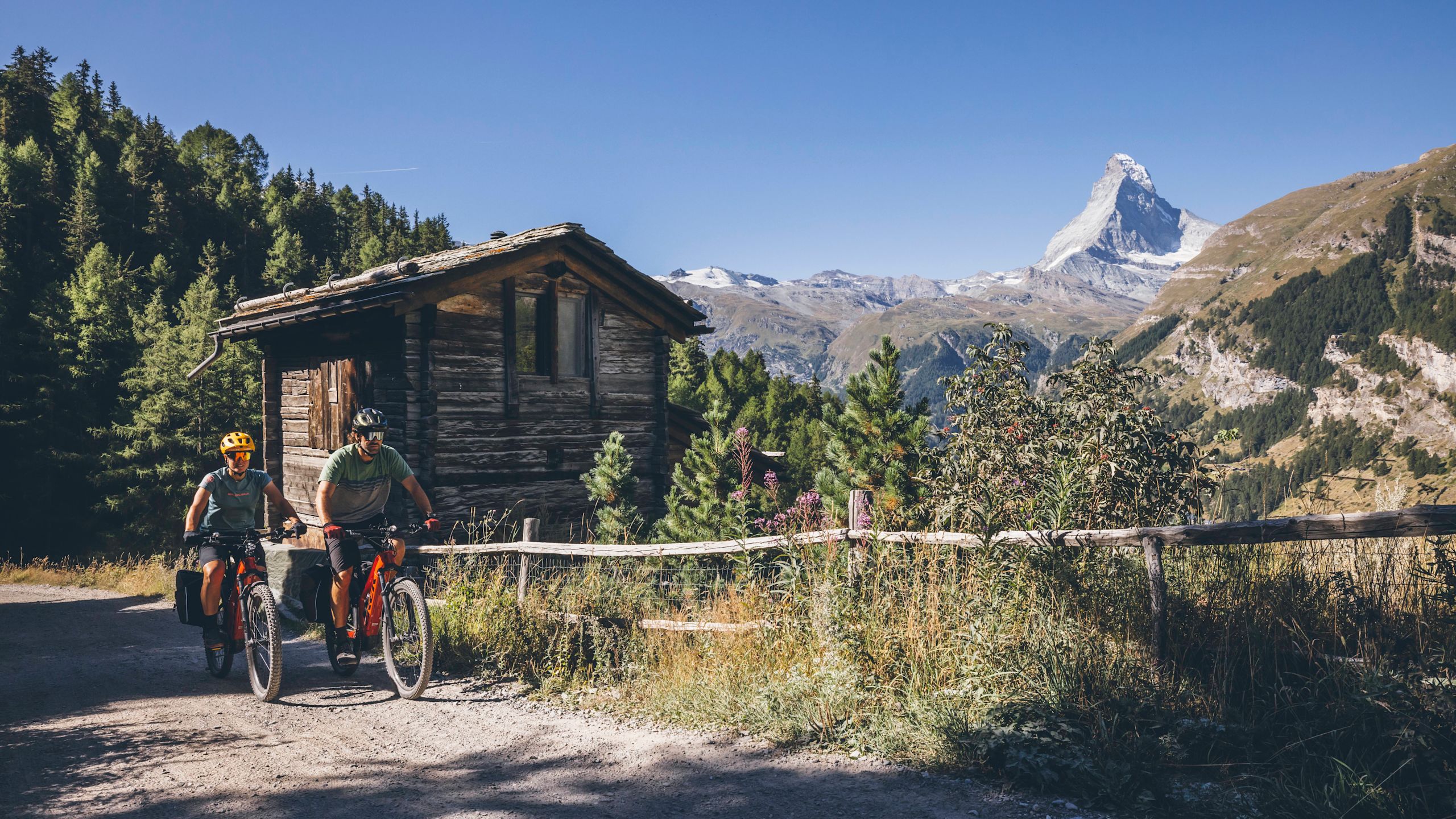 Deux vététistes sur un chemin de gravier dans les Alpes suisses avec vue sur le Cervin, suivant l’itinéraire de la Glacier Bike Tour West, Valais, Suisse