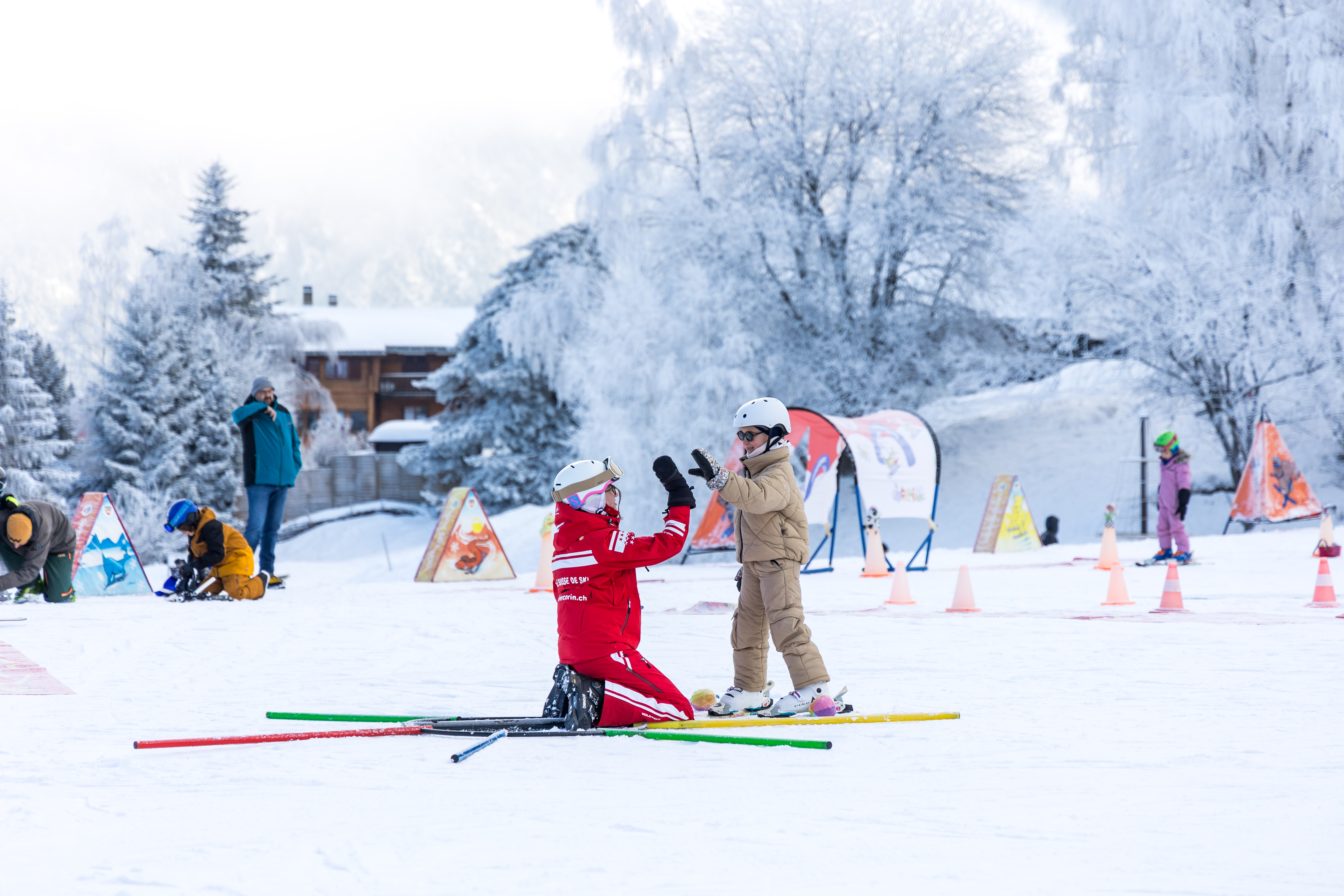 Un moniteur de ski et un enfant se donnent un high-five lors d’un cours de ski dans l’espace débutants Le Lavioz à Vercorin, en Valais, entourés d’un paysage hivernal.