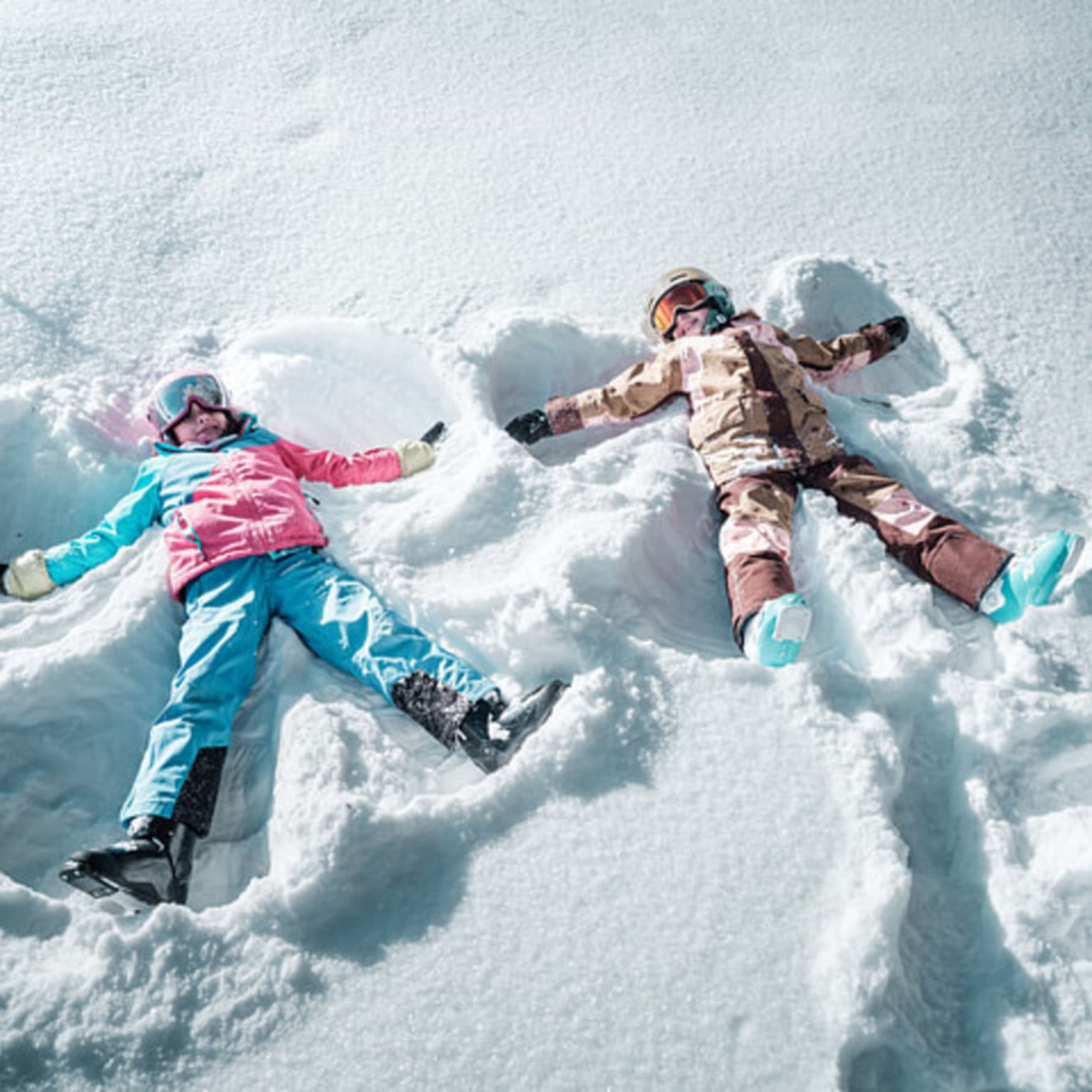Deux enfants allongés dans la neige faisant des anges au parc familial sur la Hannigalp à Grächen, entourés d’un paysage hivernal.