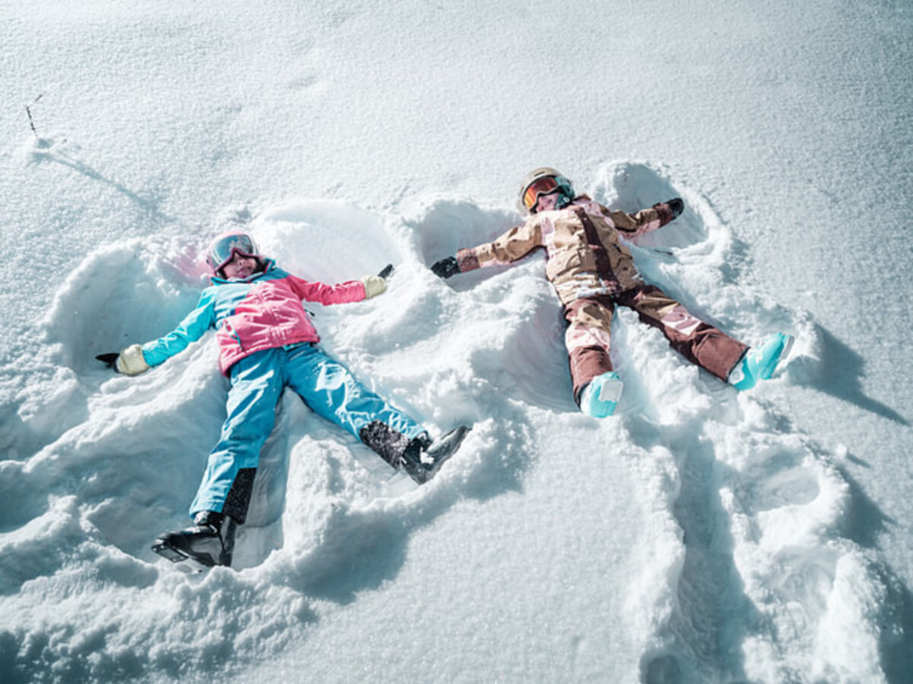 Two children lying in the snow making snow angels in the family park on the Hannigalp in Grächen, surrounded by a winter landscape.