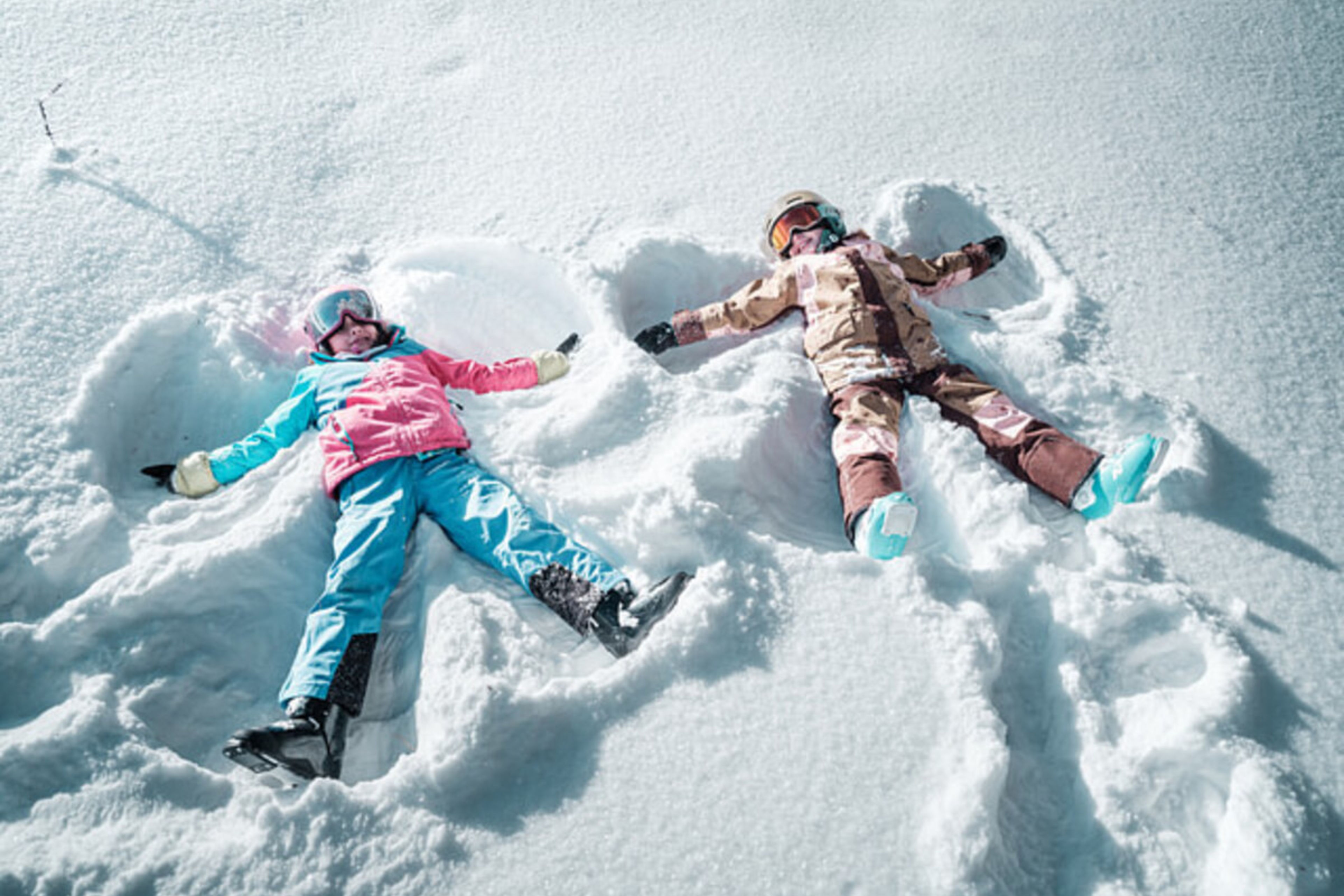 Two children lying in the snow making snow angels in the family park on the Hannigalp in Grächen, surrounded by a winter landscape.