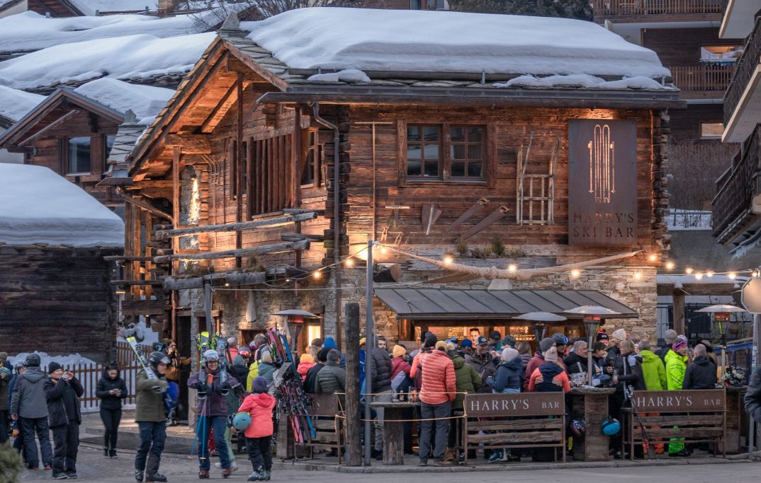 Harry’s Ski Bar in Zermatt mit vielen Gästen in Ski- und Winterkleidung vor einem beleuchteten Chalet am Abend