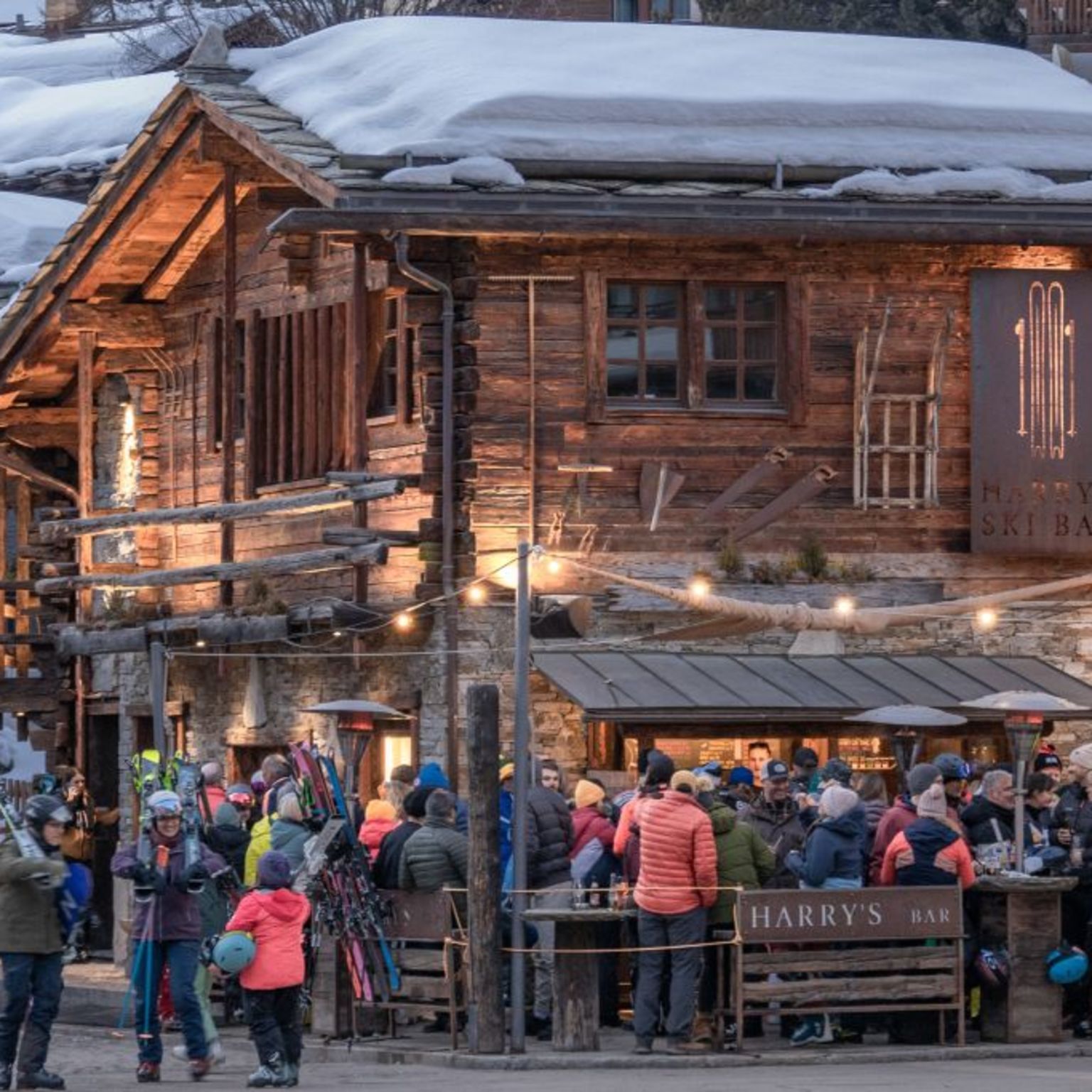 Harry’s Ski Bar in Zermatt mit vielen Gästen in Ski- und Winterkleidung vor einem beleuchteten Chalet am Abend