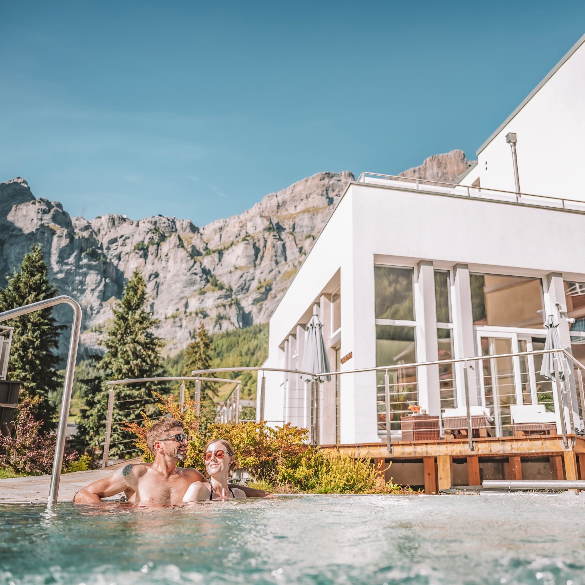 Ein Paar entspannt im Außenpool des Therme51 in Leukerbad, umgeben von Bergen und Sonnenschein