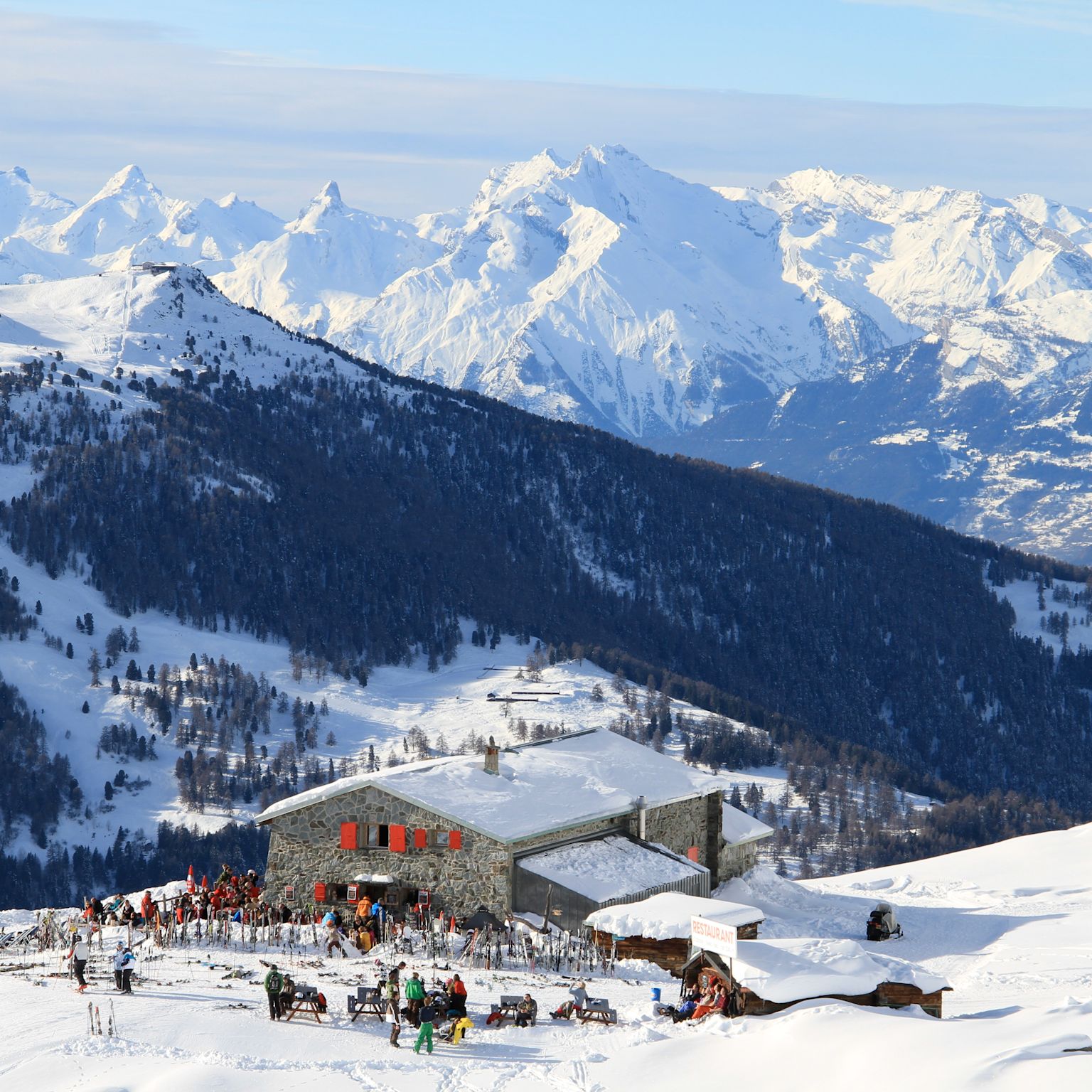 Cabane Bella-Tola restaurant in St-Luc, Valais, surrounded by snowy mountains and a sun terrace packed with skiers