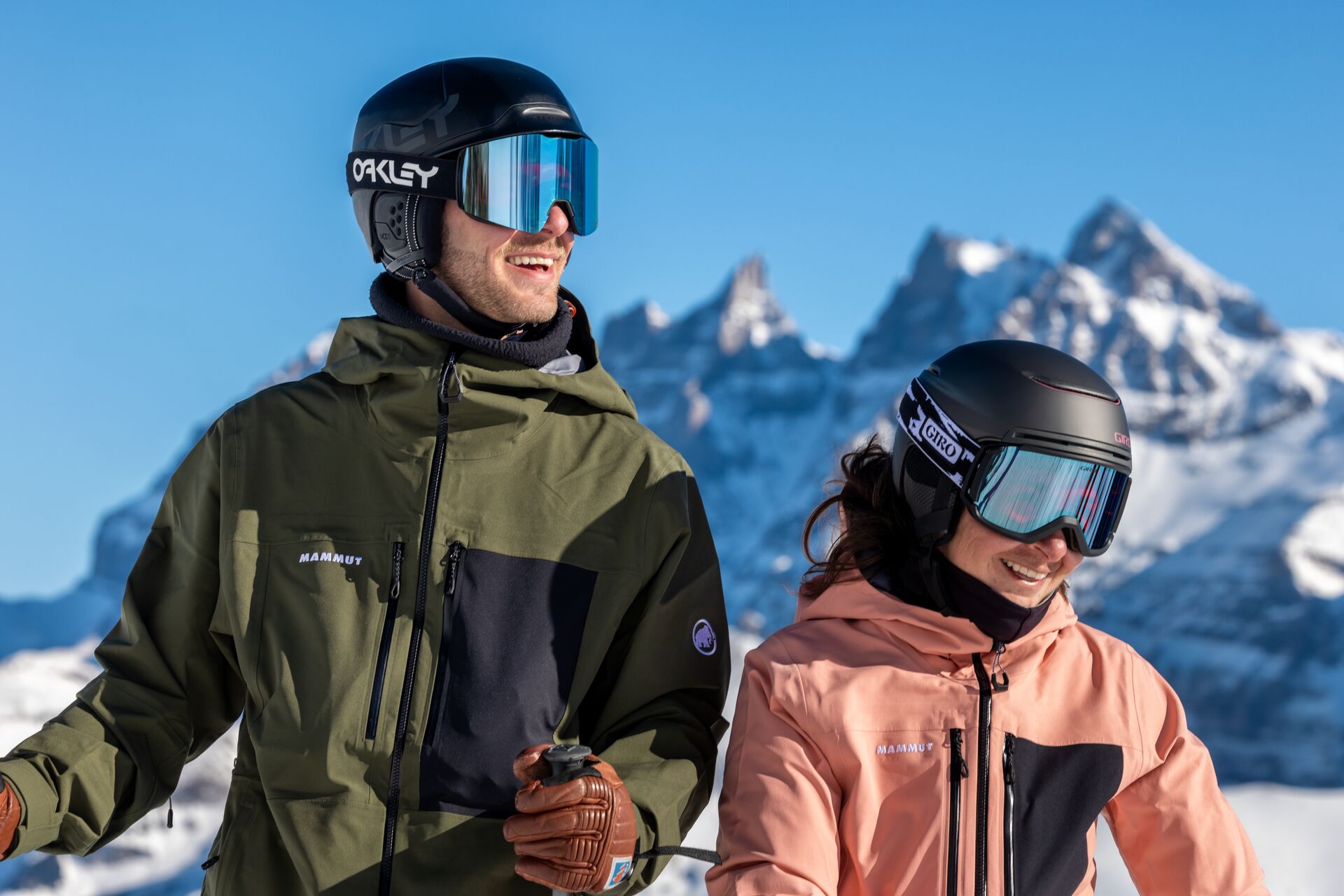Un homme et une femme souriants, casqués et équipés pour le ski, devant les Dents du Midi à Champéry