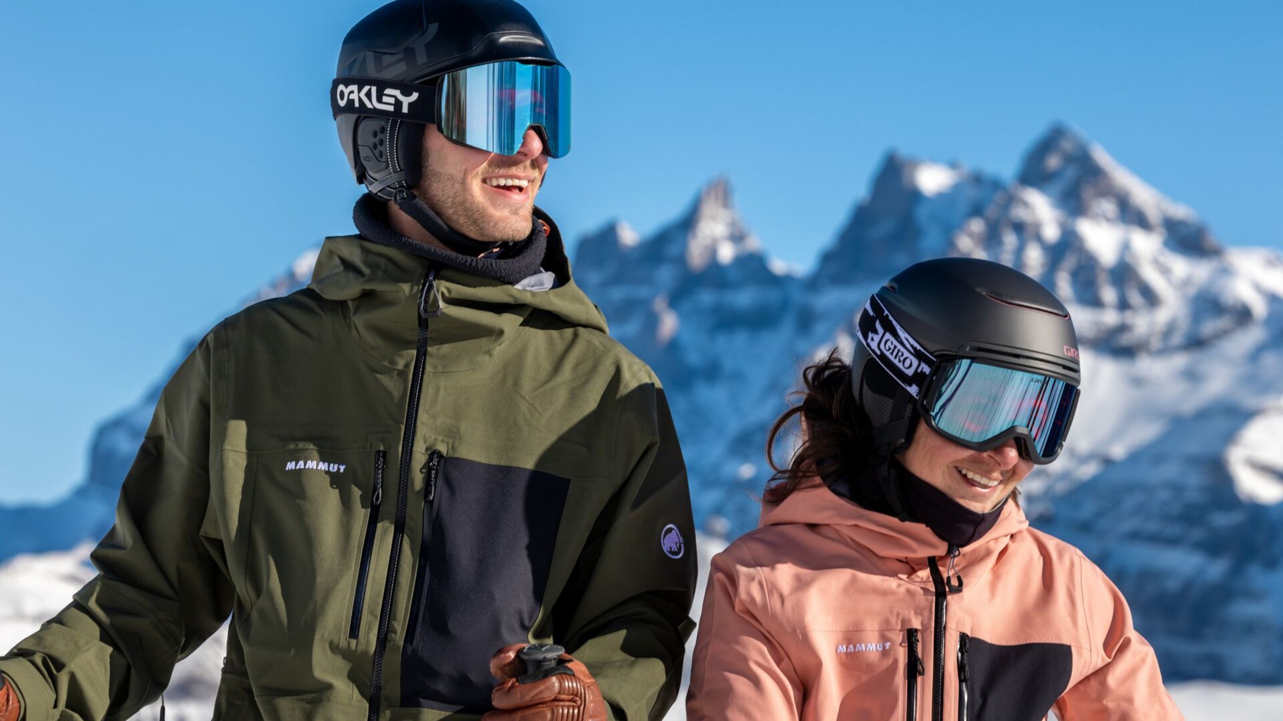 Un homme et une femme souriants, casqués et équipés pour le ski, devant les Dents du Midi à Champéry