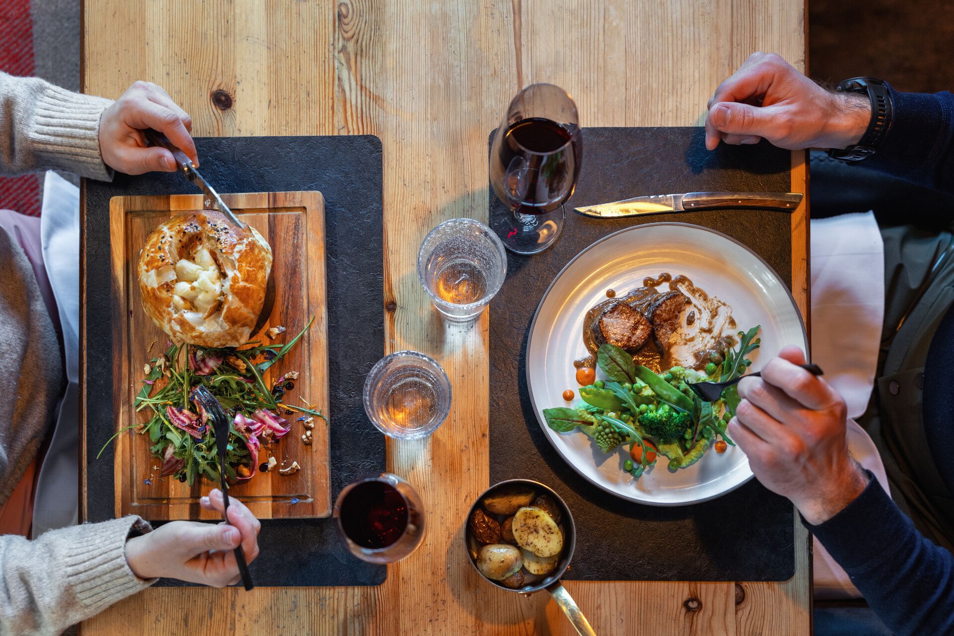 Deux personnes dégustent un dîner aux spécialités valaisannes dans un restaurant à Champéry, avec viande, légumes, pommes de terre et vin rouge